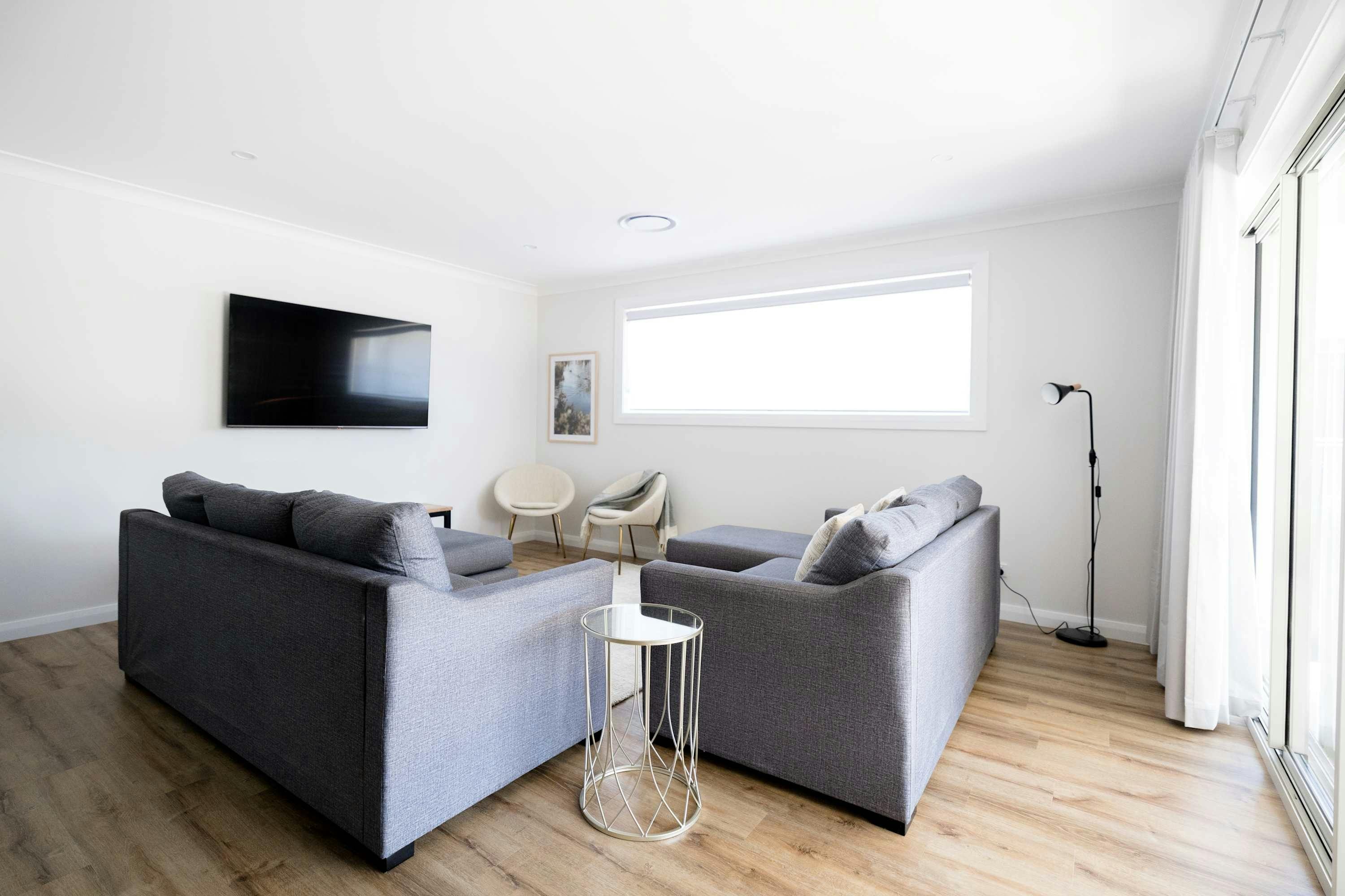 2 grey couches with a large smart tv, 2 armchairs, a lamp, white rug and coffee table.