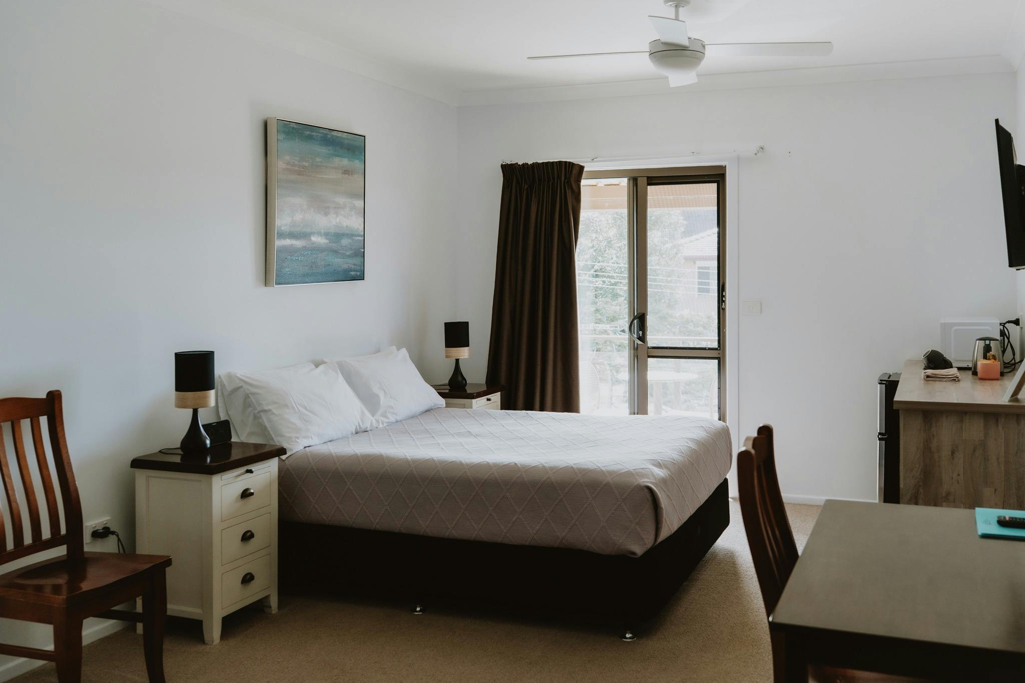 Spacious room showing chair, bedside tables and queen bed to sliding doors. Desk and kitchenette.
