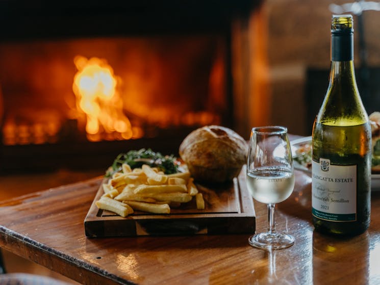 Burger, fries and bottle of wine with glass in front of a fireplace on a Kenny Escapes Winery Tour