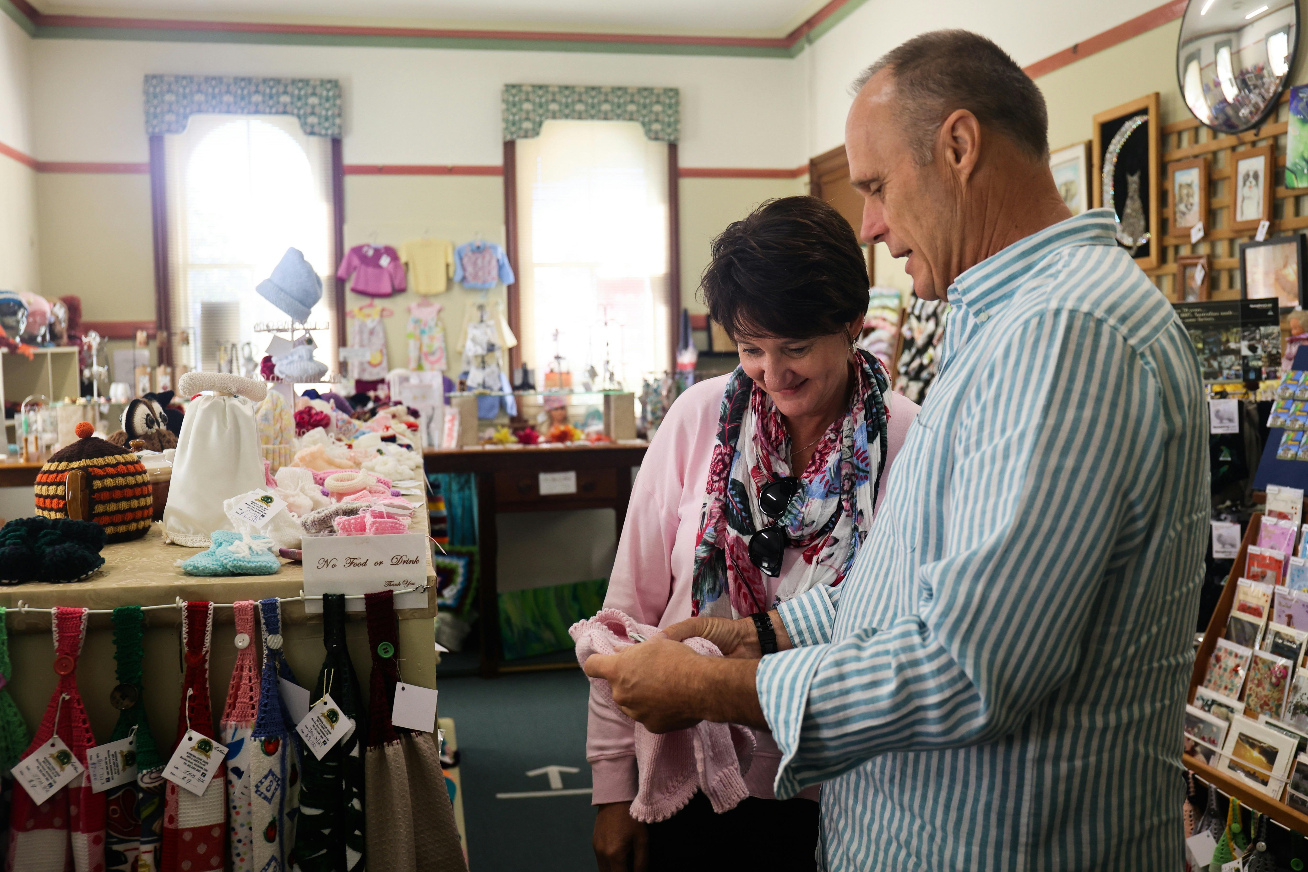 Two people looking at a handmade baby's sweater in the gift shop area of the Magistrates Tea Rooms.