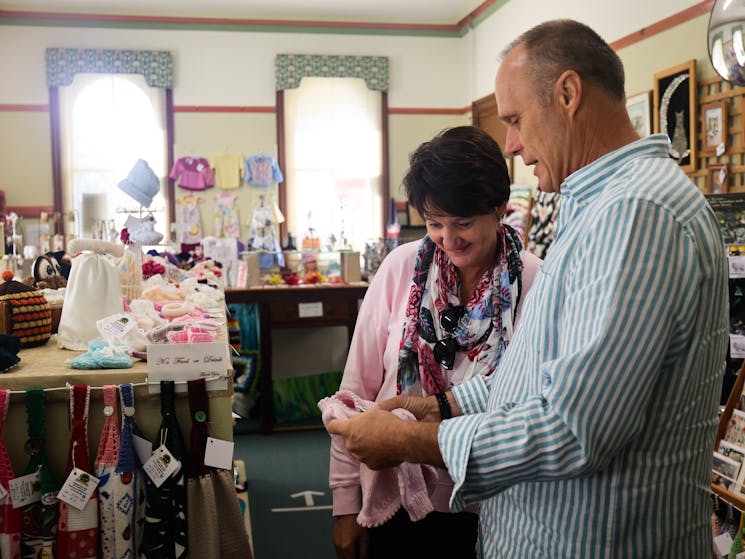 Two people looking at a handmade baby's sweater in the gift shop area of the Magistrates Tea Rooms.