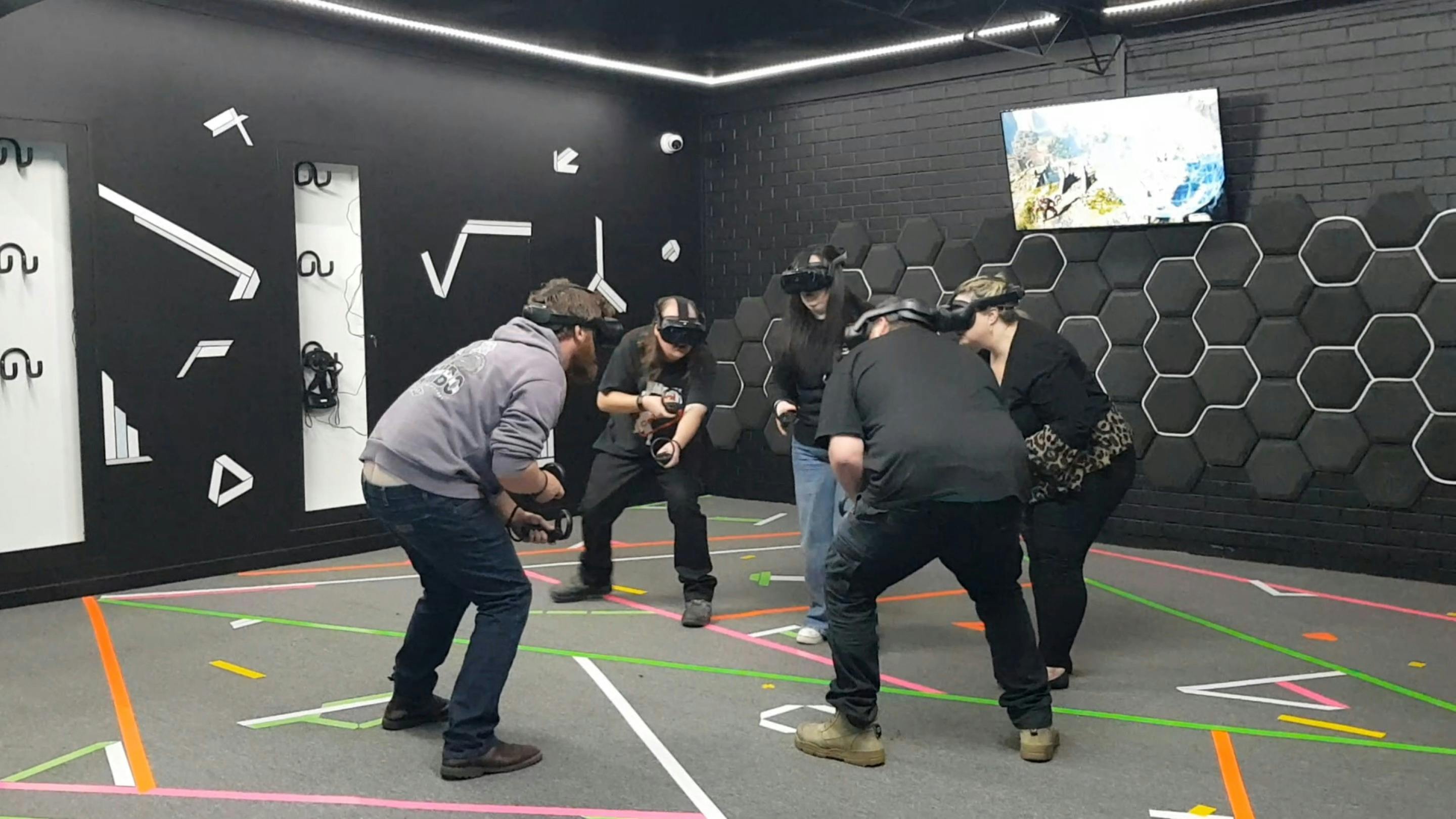Five people wearing VR headsets crouching and holding virtual objects