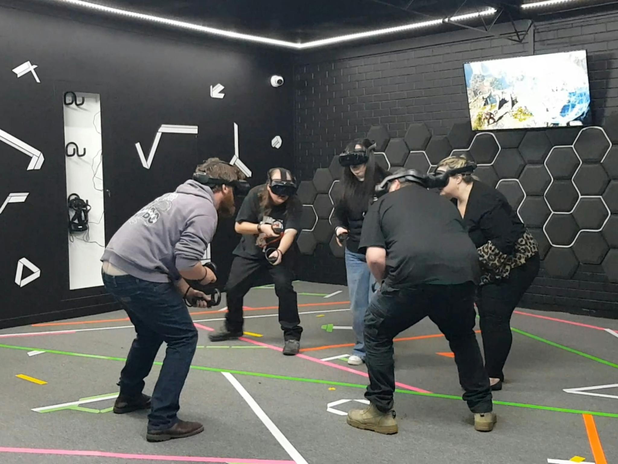 Five people wearing VR headsets crouching and holding virtual objects