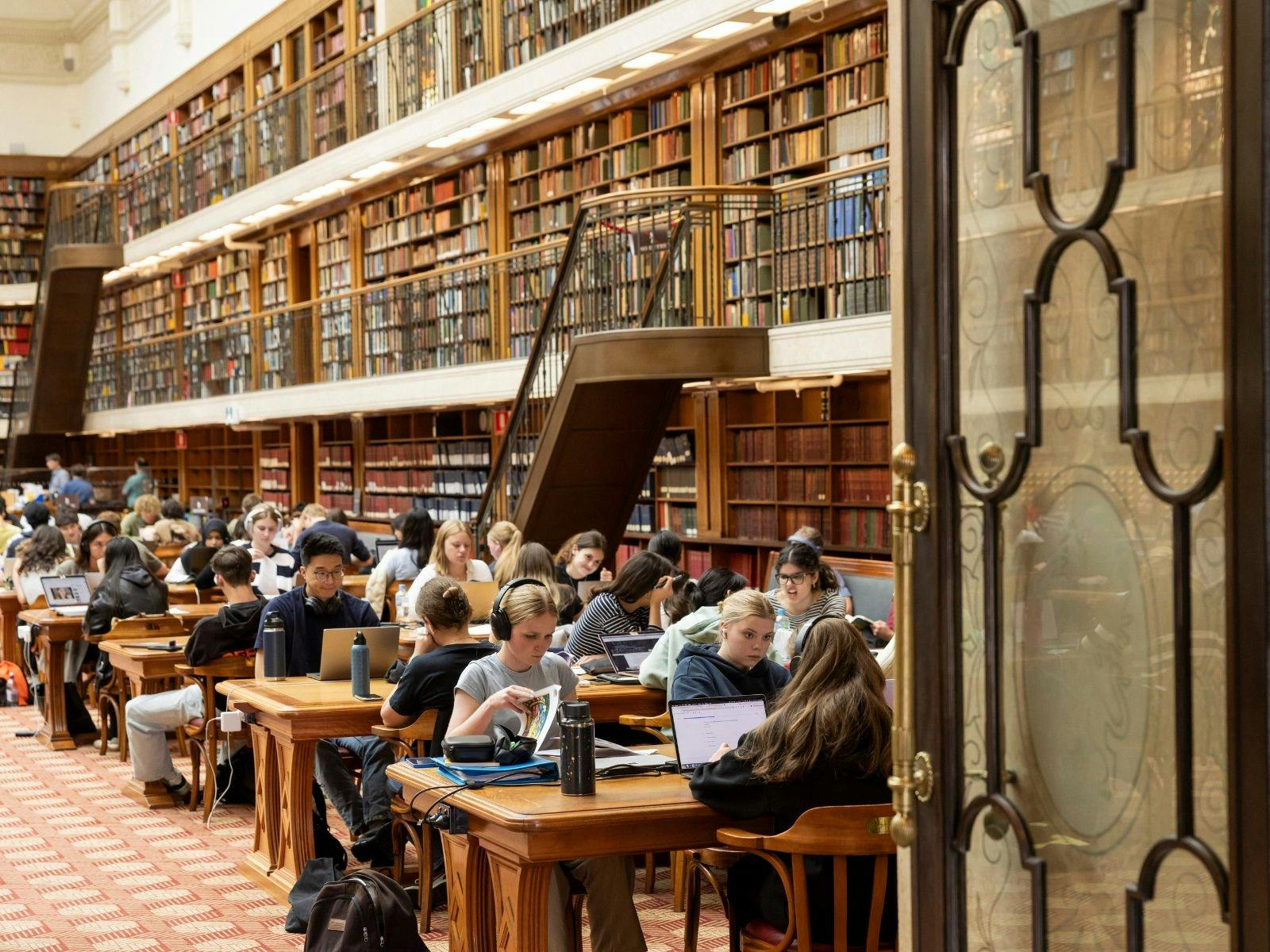 A library with  rows of desks filled with people seated and reading and studying