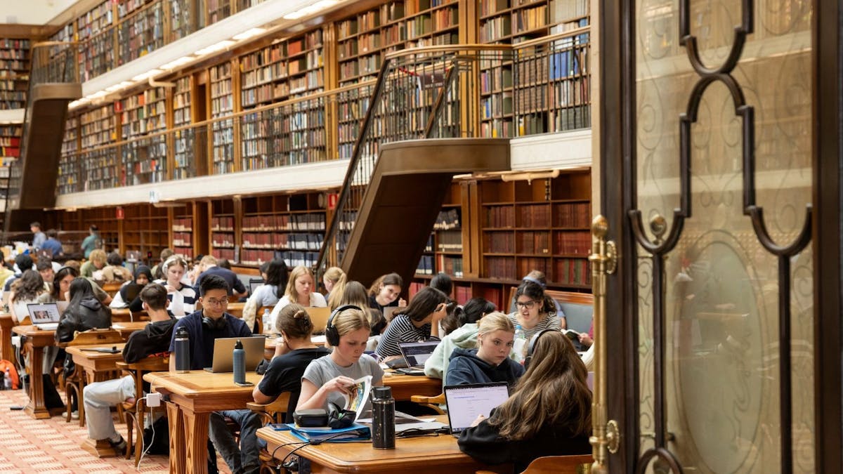 A library with rows of desks filled with people seated and reading and studying A library with rows of desks filled with people seated and reading and studying