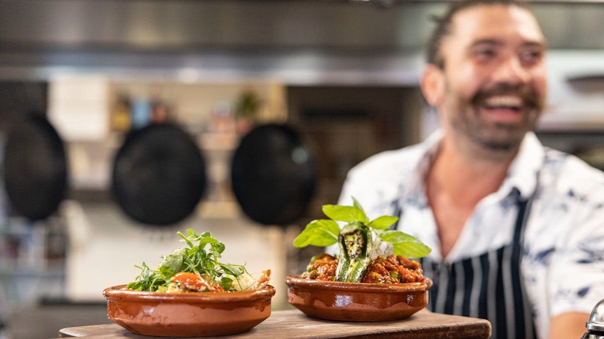 Head Chef Evan smiling with Garlic & Chilli prawns and lamb albondigas (meatballs) in the pass