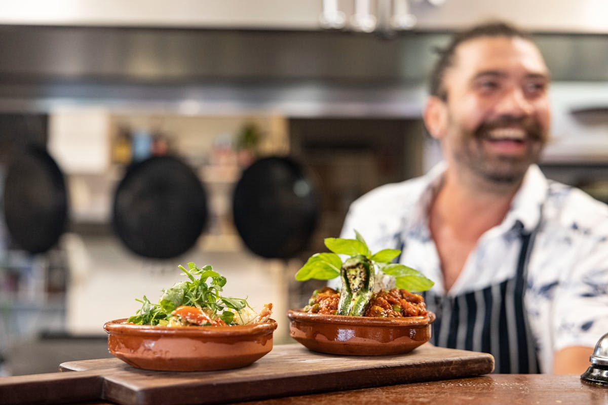 Head Chef Evan smiling with Garlic & Chilli prawns and lamb albondigas (meatballs) in the pass