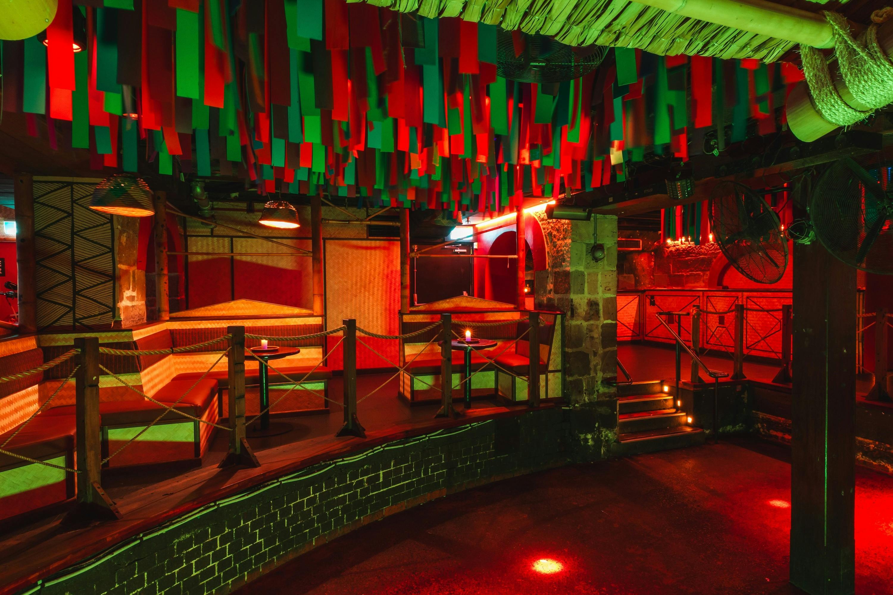 Colourful nightclub with bamboo booths and a dance floor under hanging red and green strips