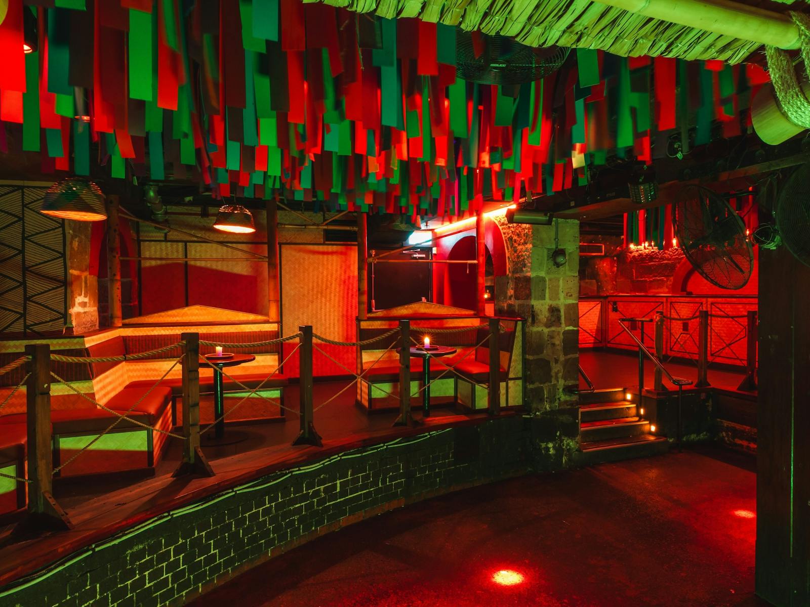 Colourful nightclub with bamboo booths and a dance floor under hanging red and green strips