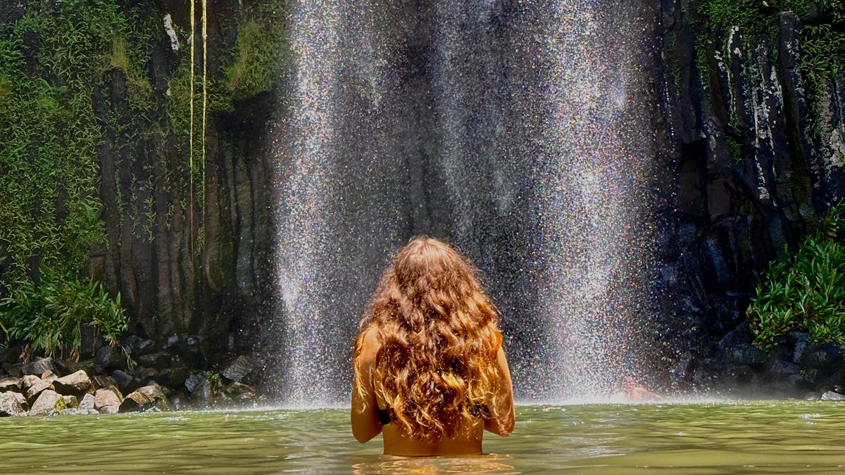 Woman standing in the water in front of Millaa Millaa Falls on the Atherton Tablelands