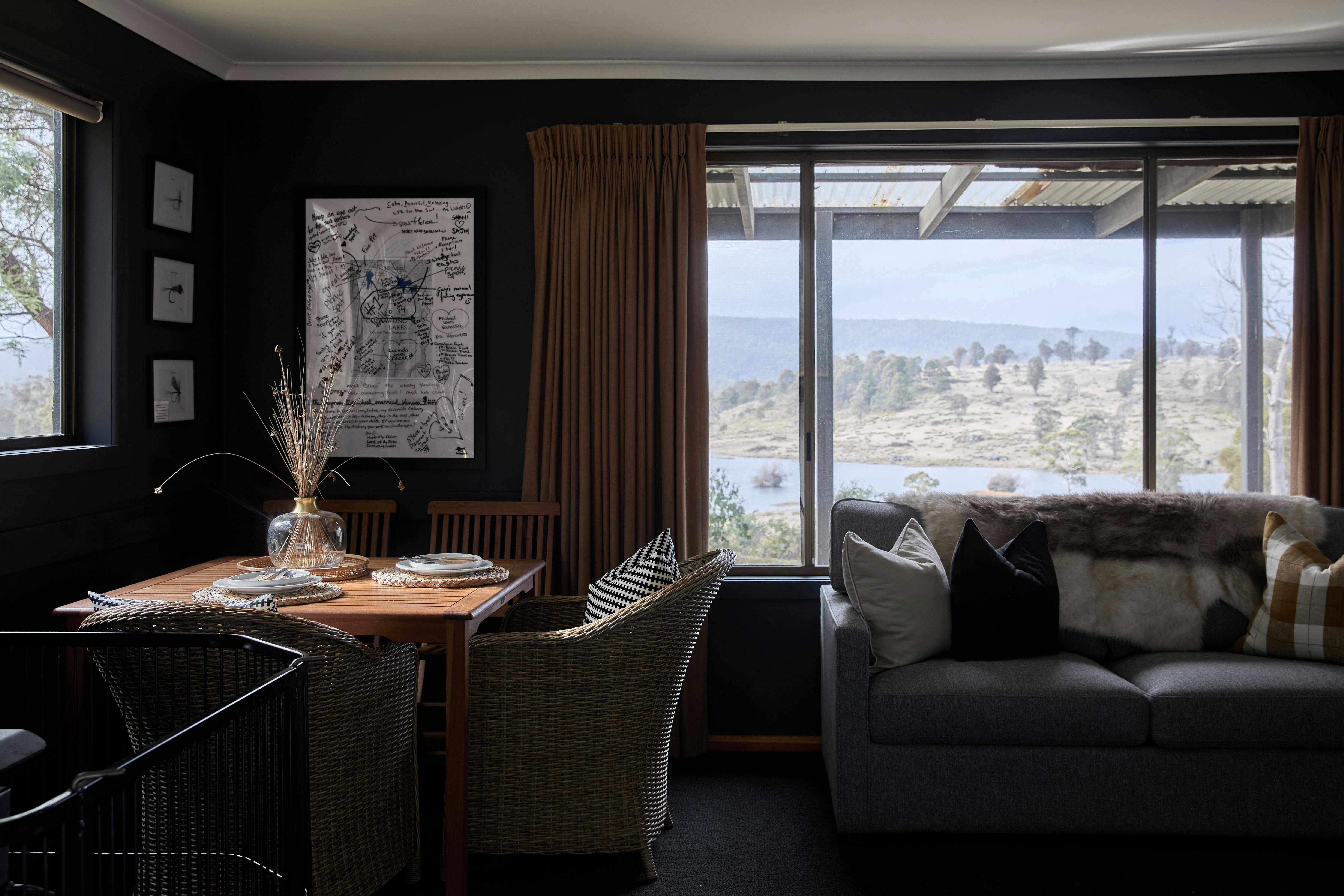 Small dining table in left corner next to couch with large window overlooking bush and lake