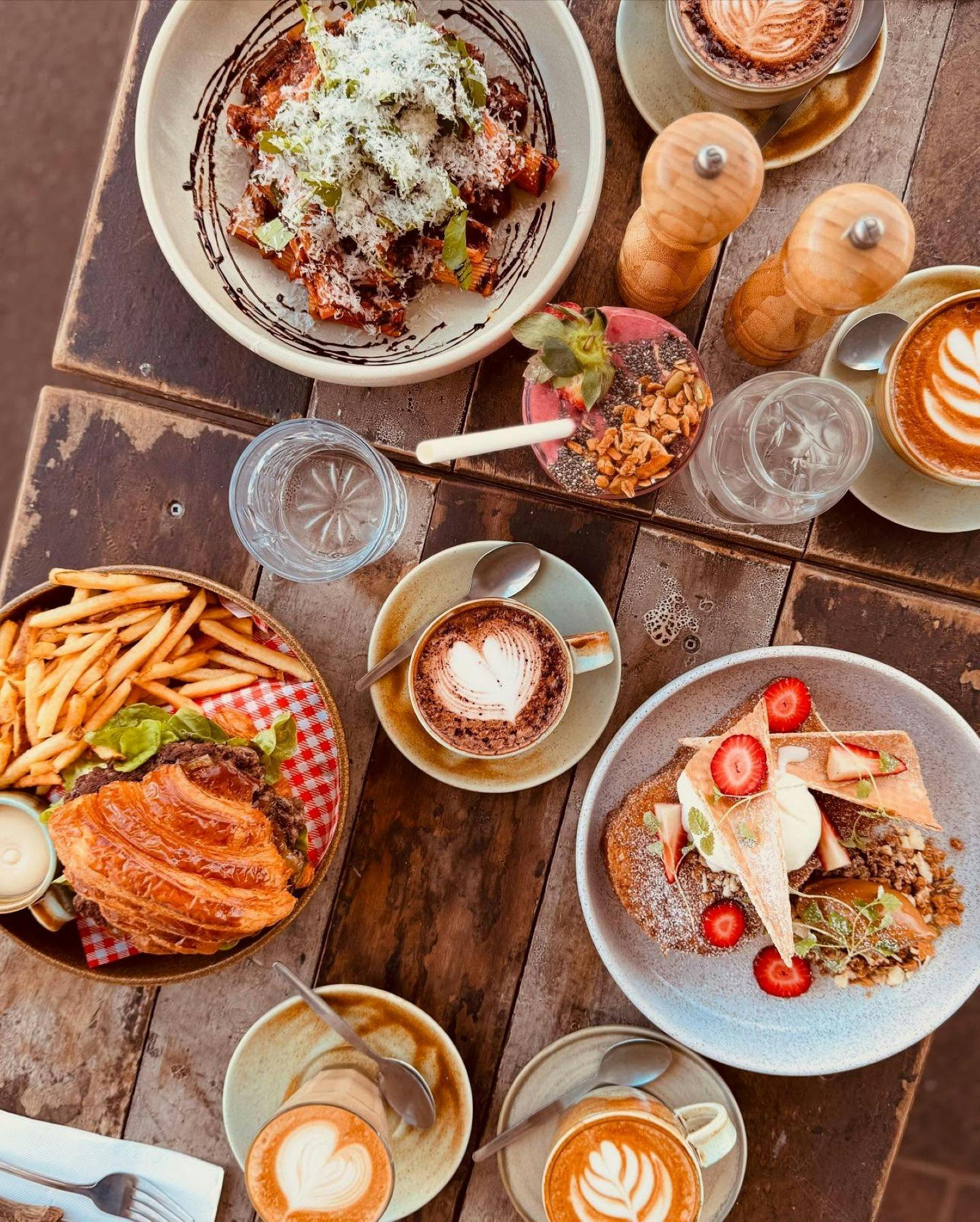 Table of delicious cafe foods: coffee, fruitshake, sweets and savouries.