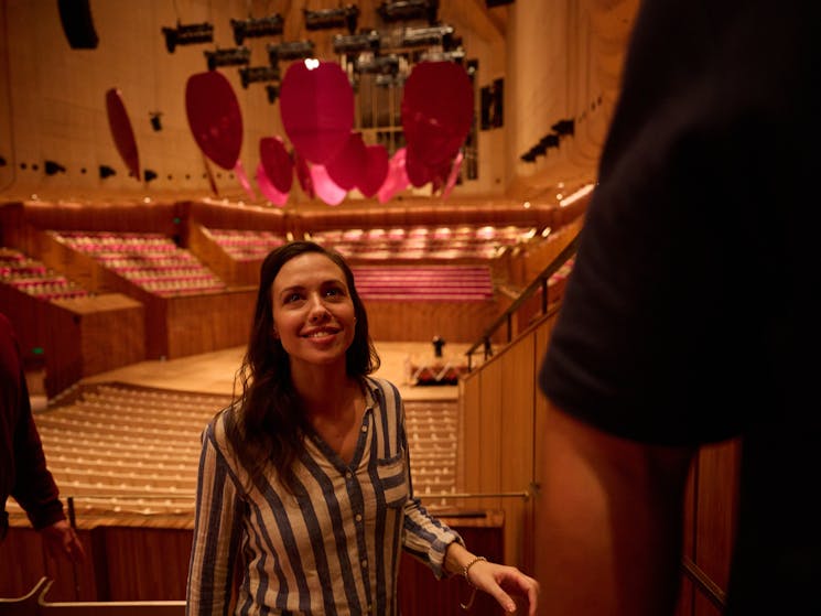 Woman with long brown hair in a blue and white shirt is walking up the stairs in the Concert Hall