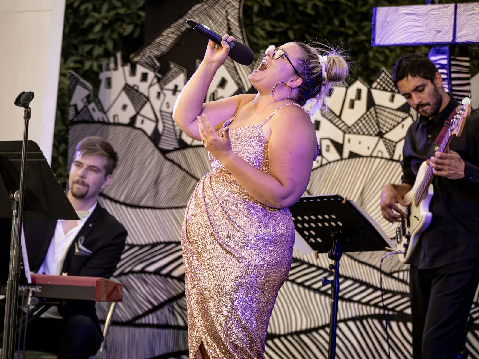 A woman in a sparkly dress belts a powerful note on stage, her expression full of emotion.