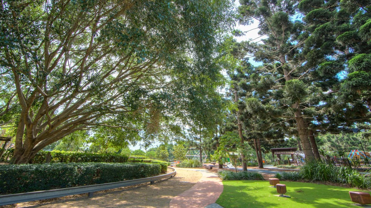 Shaded play area and pedal powered train track under large trees at Pine Rivers Park