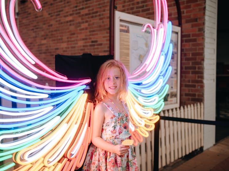 Girl standing in front of lit up colourful wings