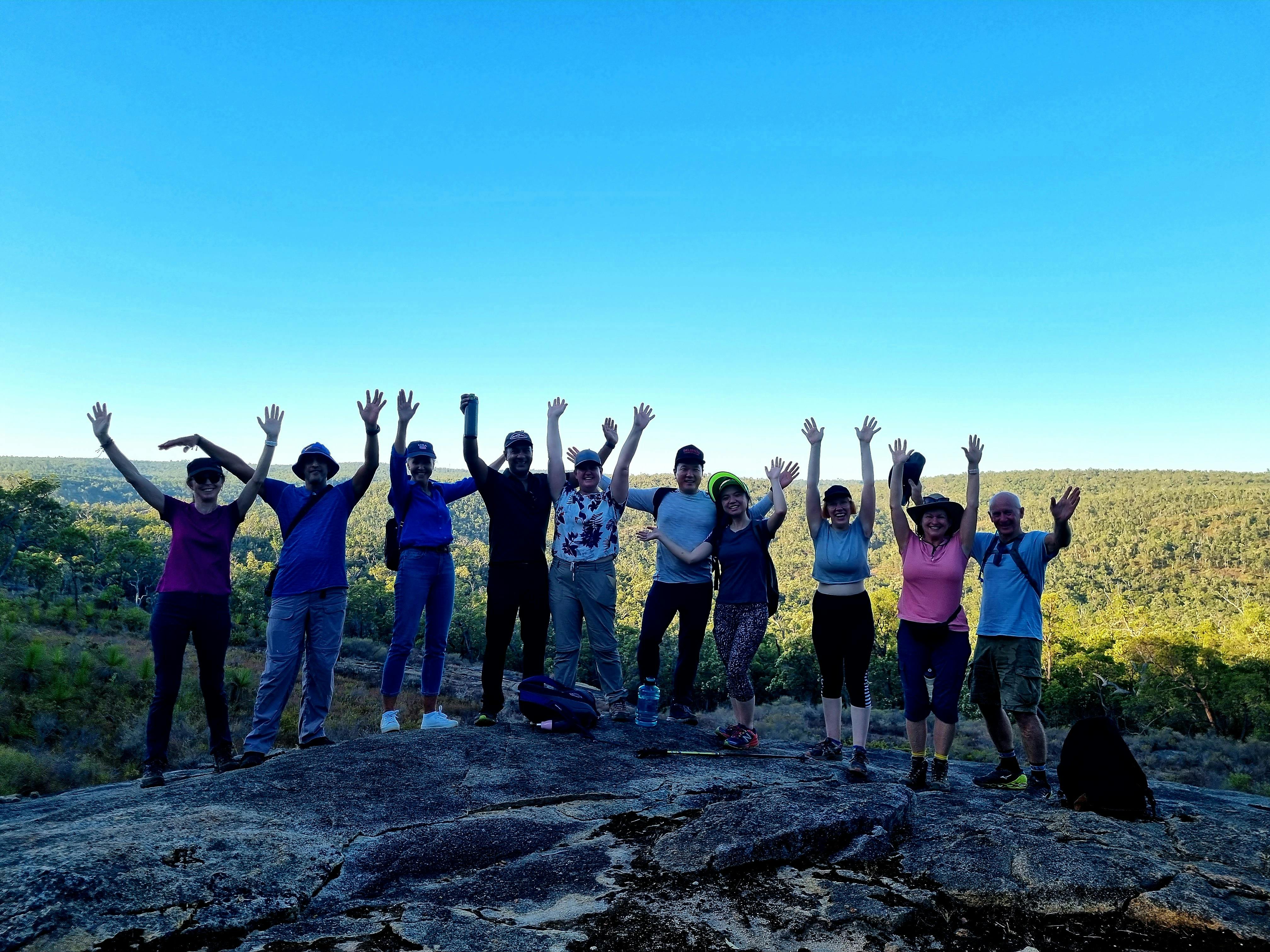 Hiking group of 10 hikers posing for the camera with their arms up in celebration