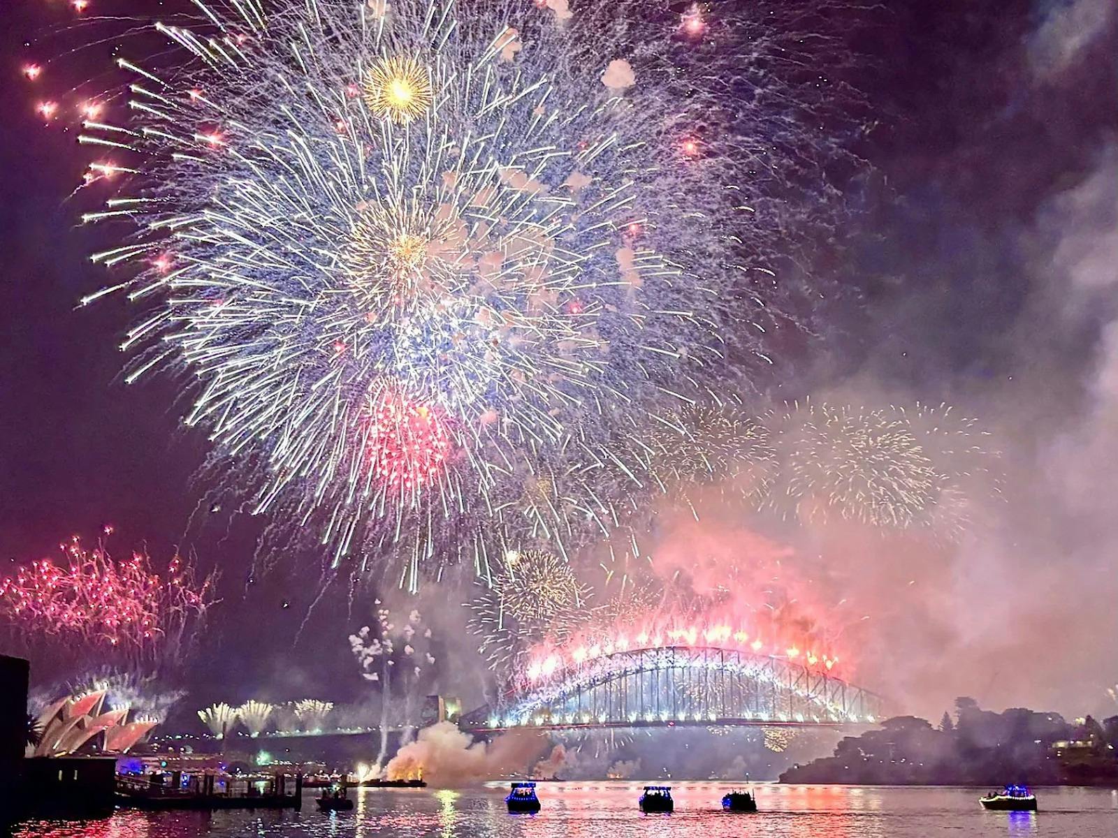 Pink and silver fireworks above the Sydney Harbour Bridge, with small boats on the water below