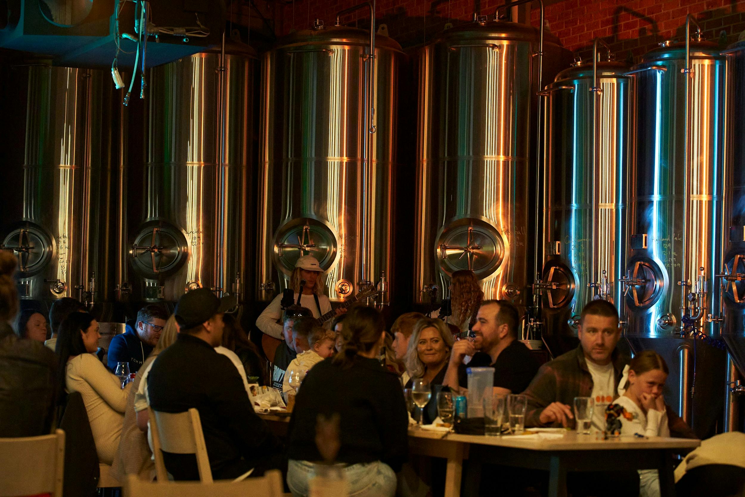 Patrons enjoying a beer at night while the fermenters in the background are lit up with lighting
