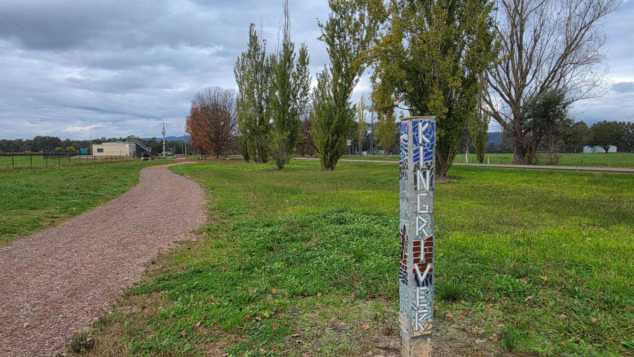 A gravel trail along green grass with a post that says 'King River' in mosaics.