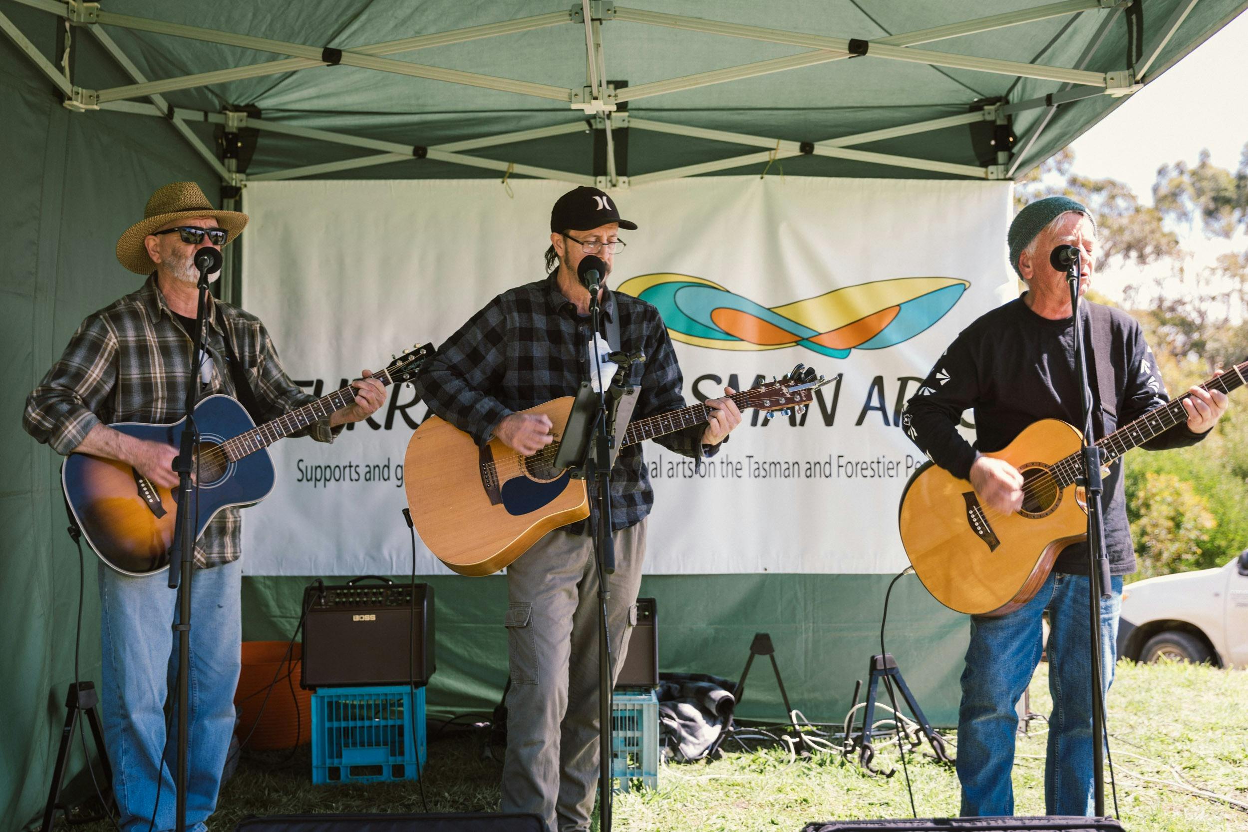 Three men on guitars perform inside a marquee.