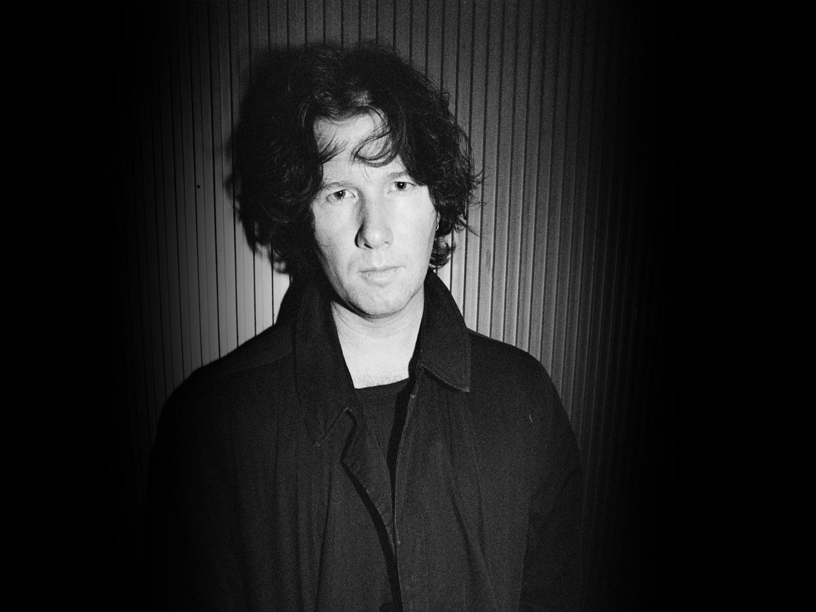 Black and white photo of Marc Dwyer standing in front of a striped wall.lle