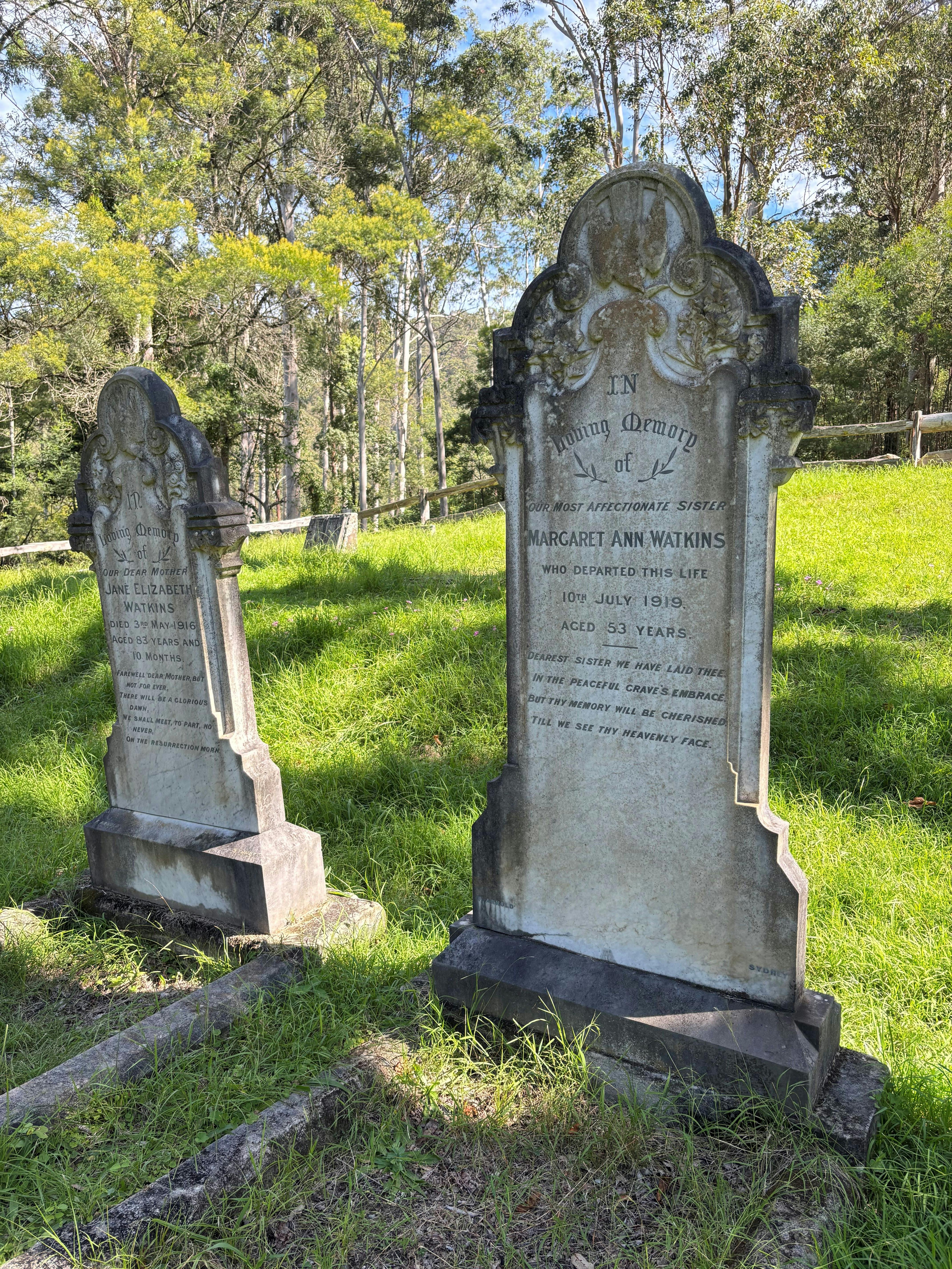 Two marble grave stones standing in a small cemetery amongst Australian gum trees.
