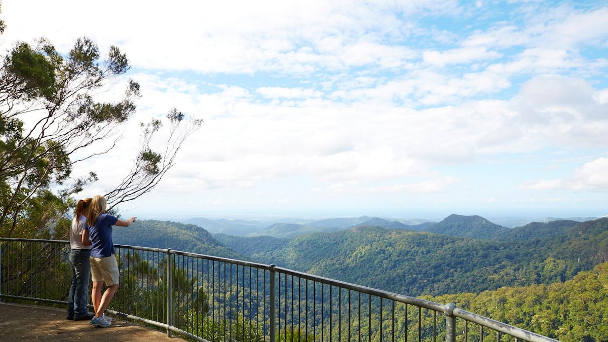 Two people standing at a lookout looking over a valley to the coast.