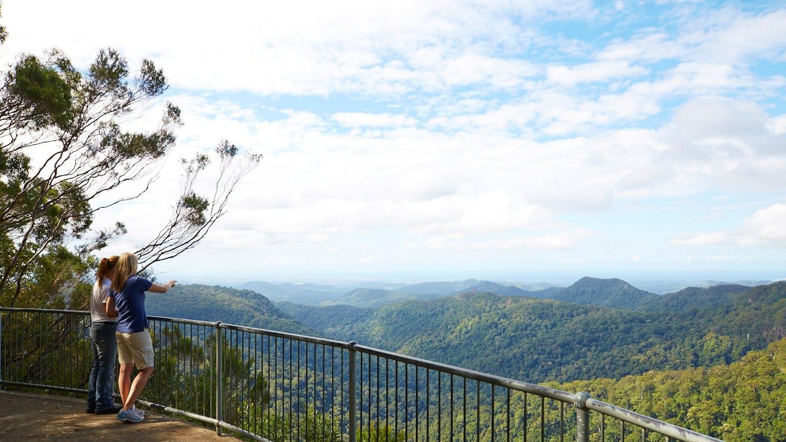 Two people standing at a lookout looking over a valley to the coast. Two people standing at a lookout looking over a valley to the coast.