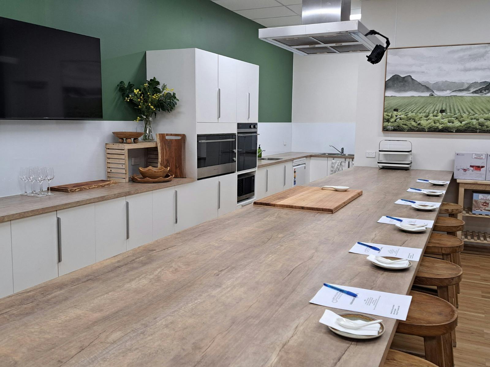 Long bench set with place settings and recipe booklets. Video projection onto TV with ovens visible.