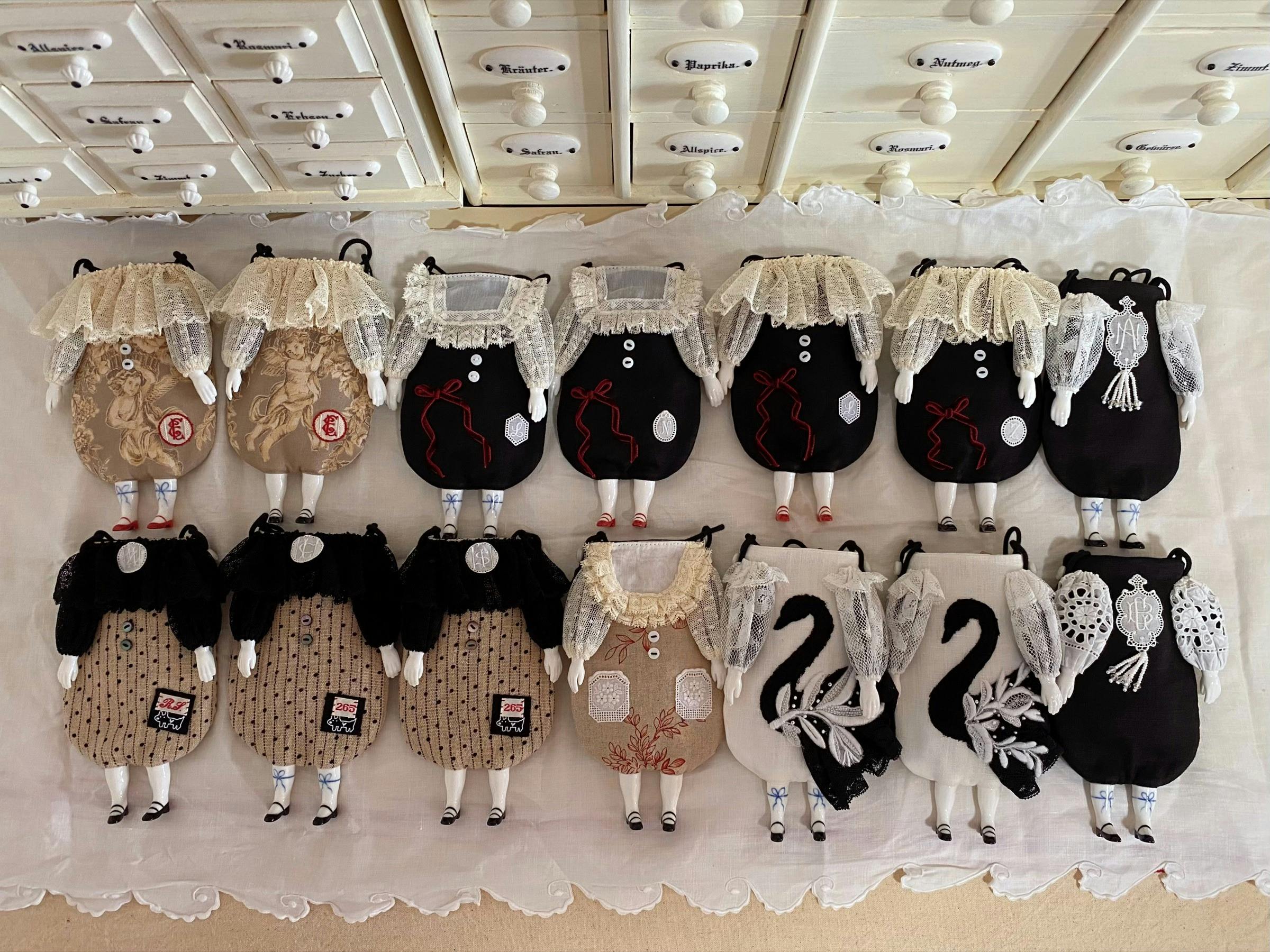 Rows of handmade black, cream and brown textile character bags with lace details.