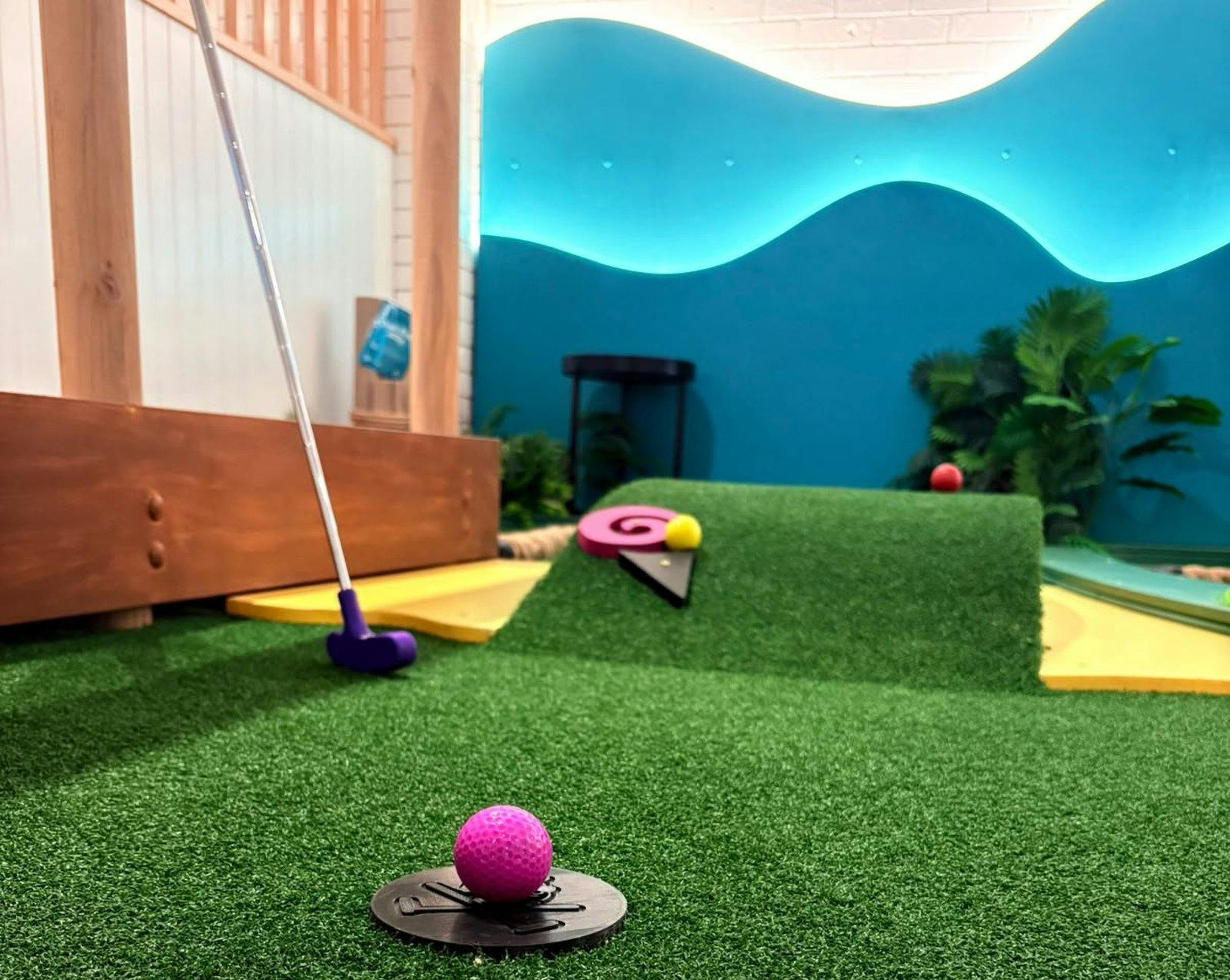 Pink golf ball on a mini golf green beside a purple putter.