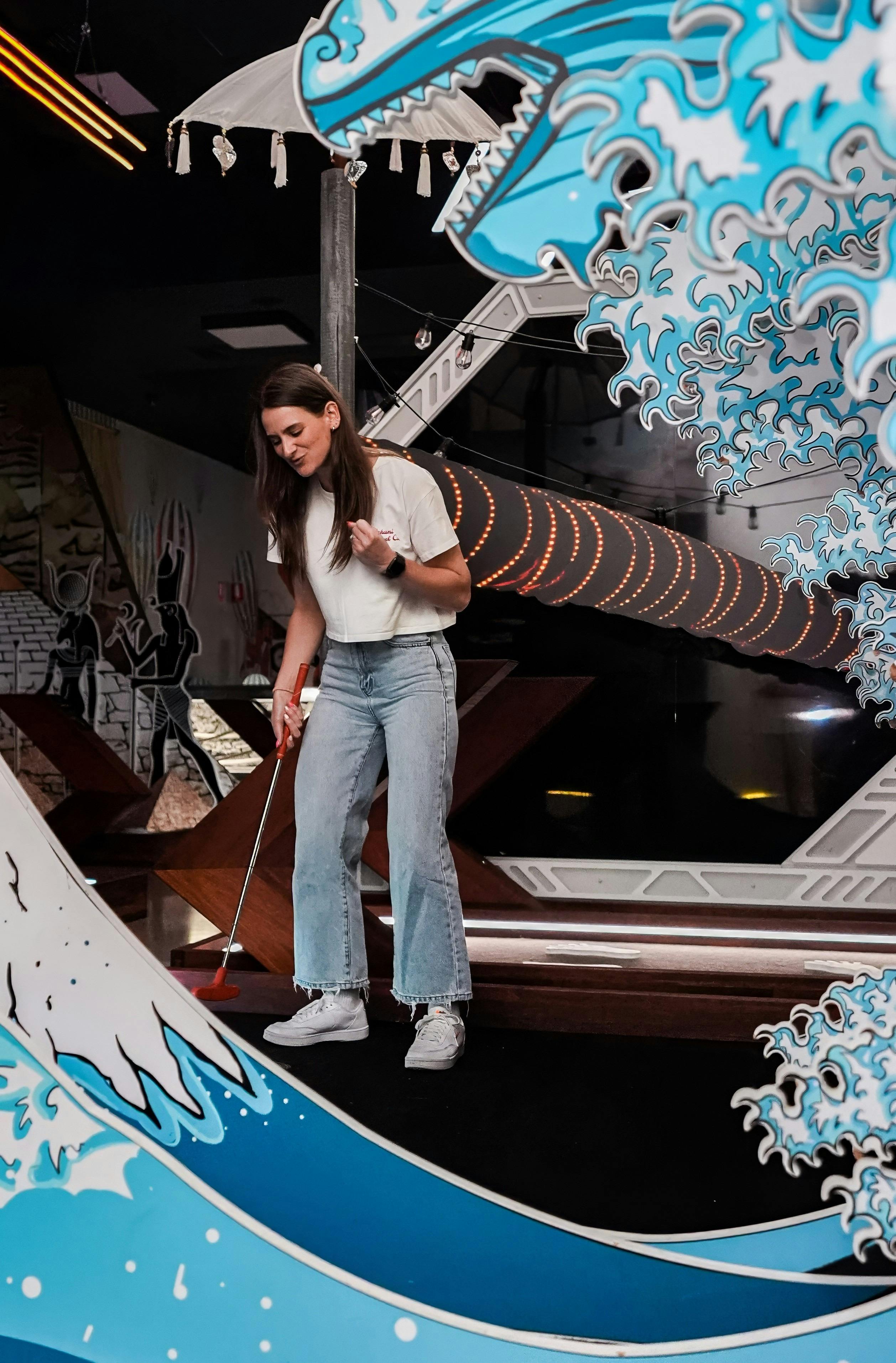 A woman celebrates on a wave themed indoor mini-golf course.