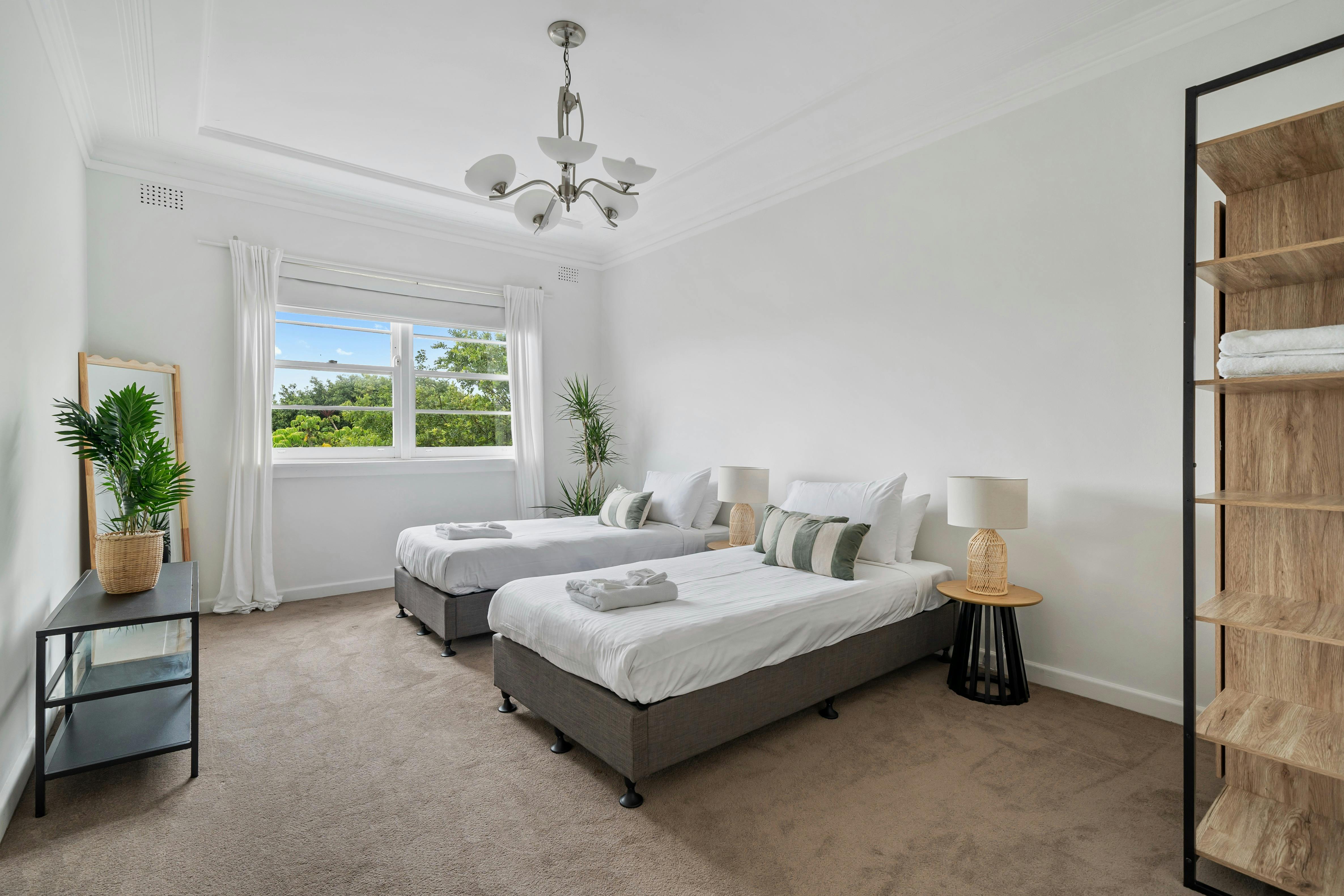 一间双床卧室，配有舒适的床、植物和透过窗户的自然光。