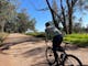 Cyclist riding on gravel green grass, gum trees, blue sky