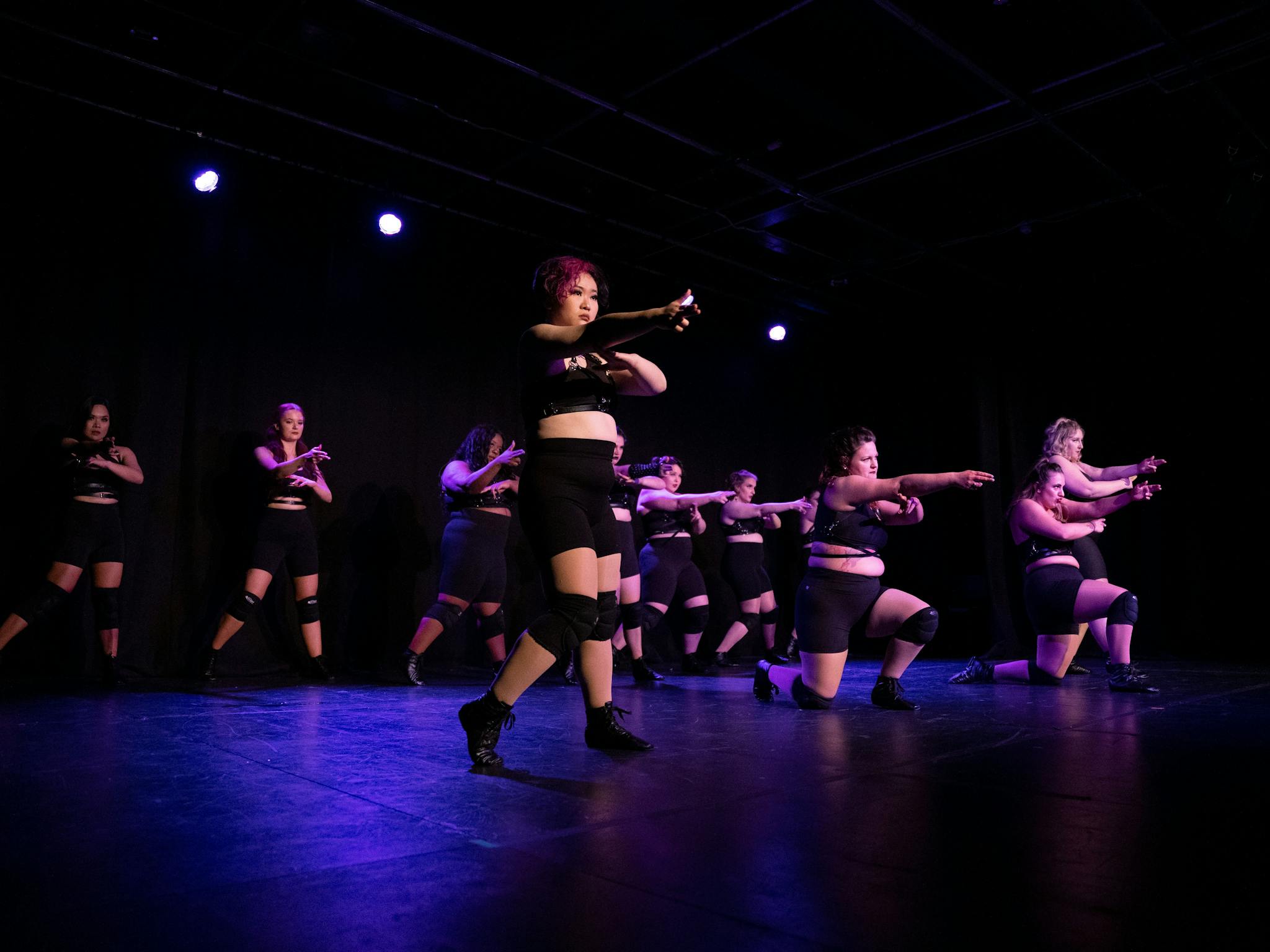 Performers in black clothes on stage in formation holding strong poses