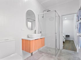 View of bathroom including floating vanity and handbasin, oval mirror, rain shower opening to b/room
