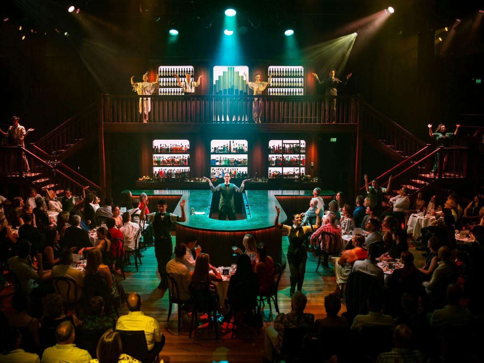 A full theatre with green lights and a set that looks like a vibrant bar.
