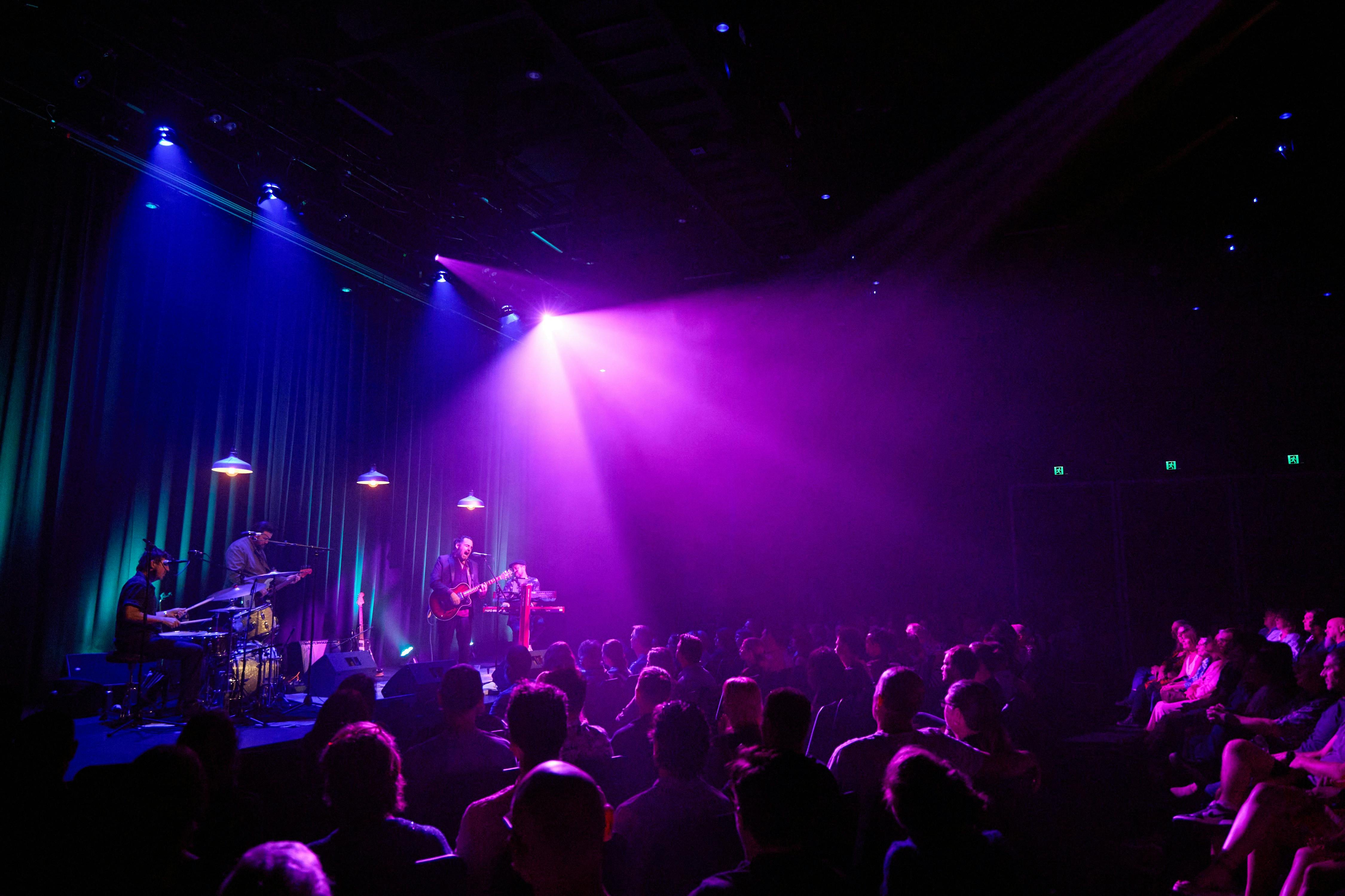 Alex Lloyd and his band play before a full crowd of seated people in the Belco Arts Theatre.