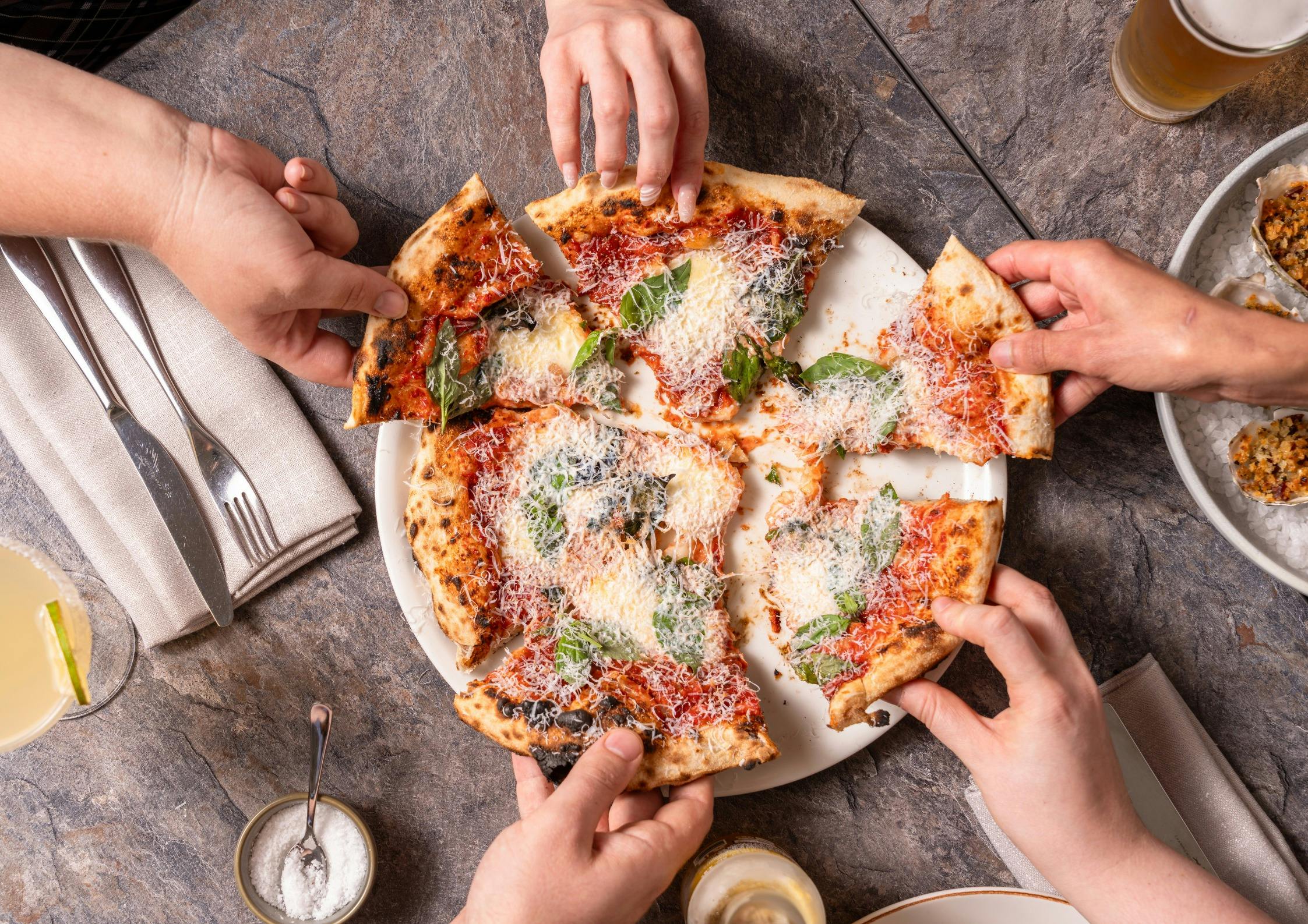 Hands reaching to grab and share a margherita pizza
