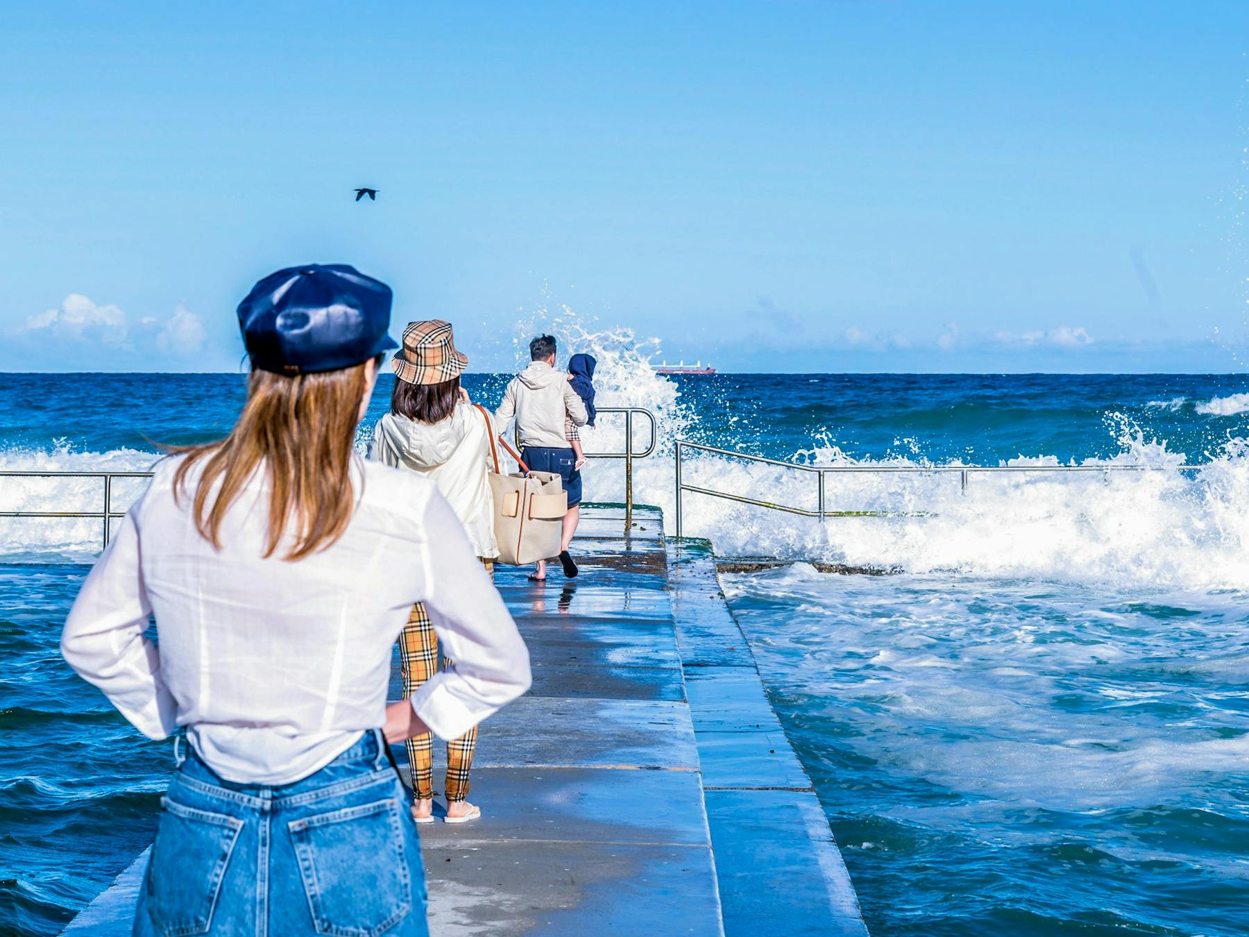 Adults walk towards the ocean waves on a nearby path
