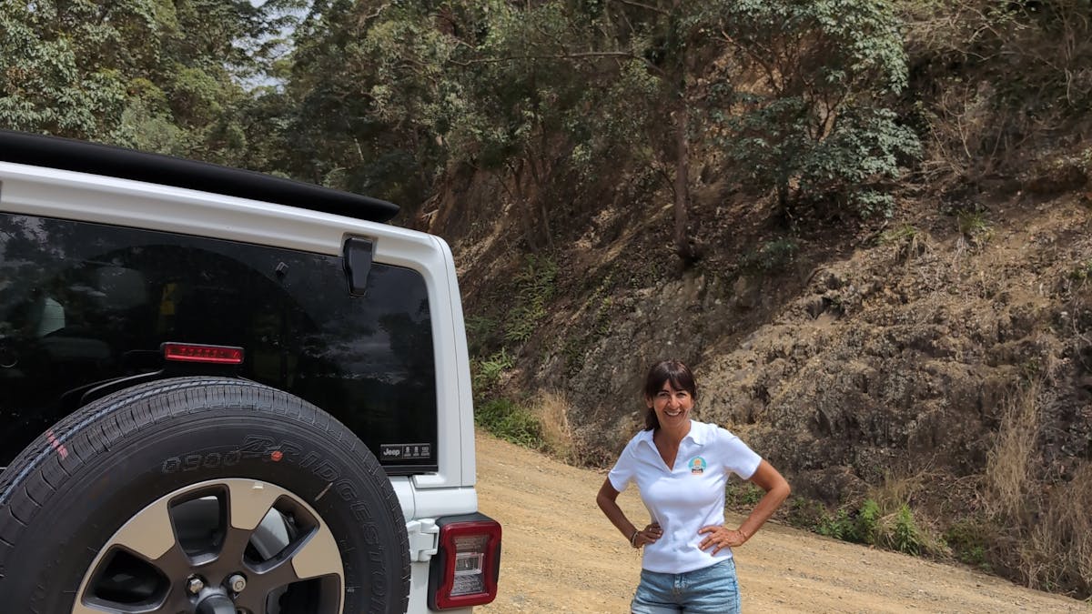 Sunny Jeeps, with Luisa the tour guide standing next to the Jeep on a hill. Looking at Hinterland.