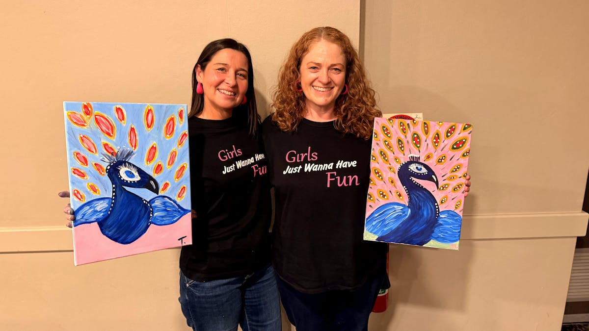 Two Paint Juicy guests smiling with their finished peacock artwork