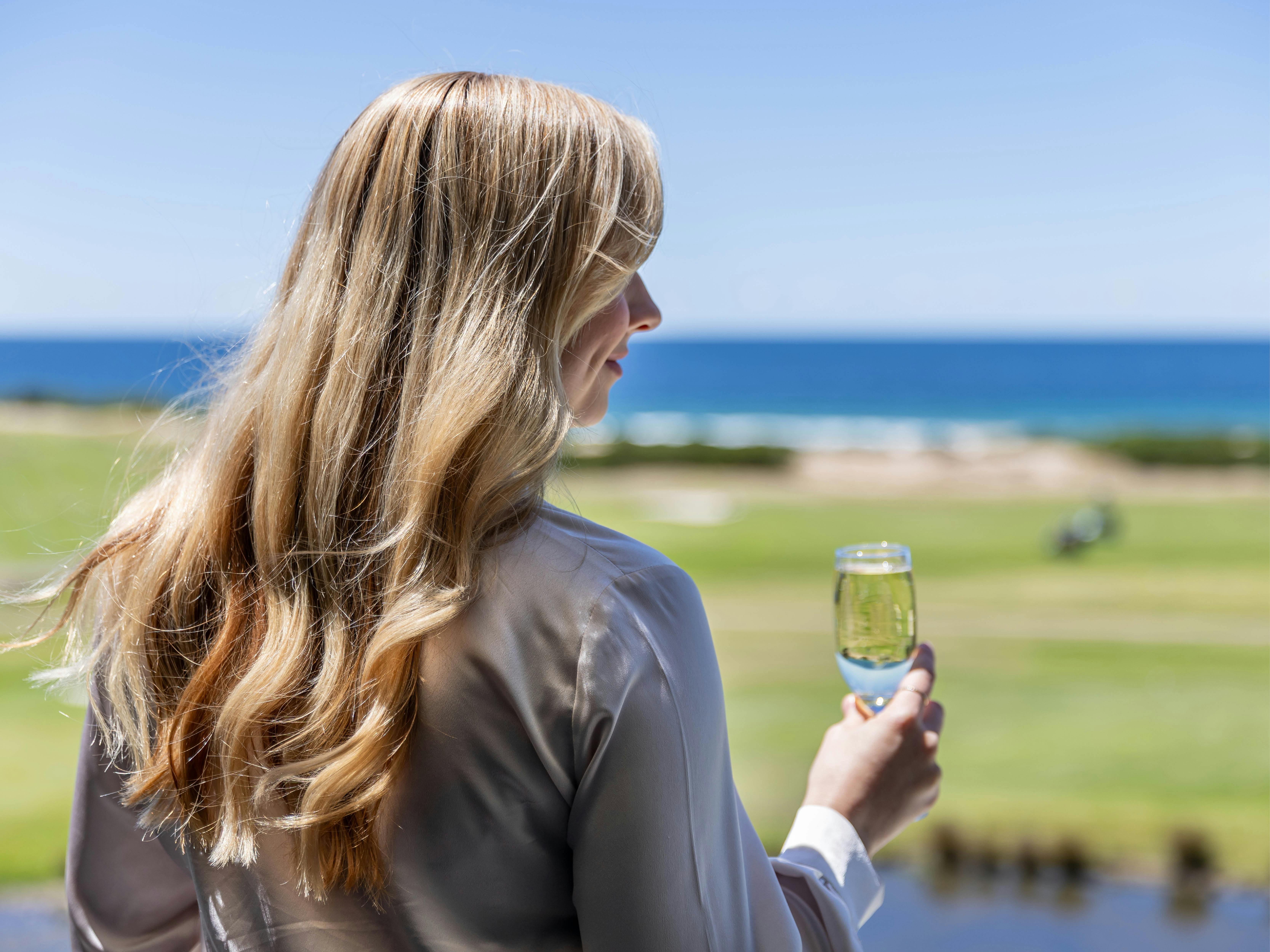 コースと海を見下ろしながらシャンパンを持つ人