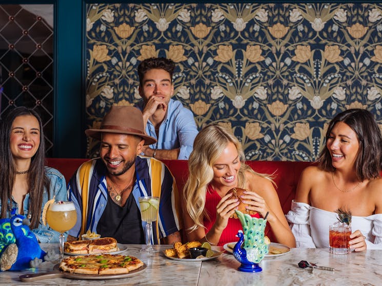 Group of five men and women eat burgers and drink cocktails together laughing