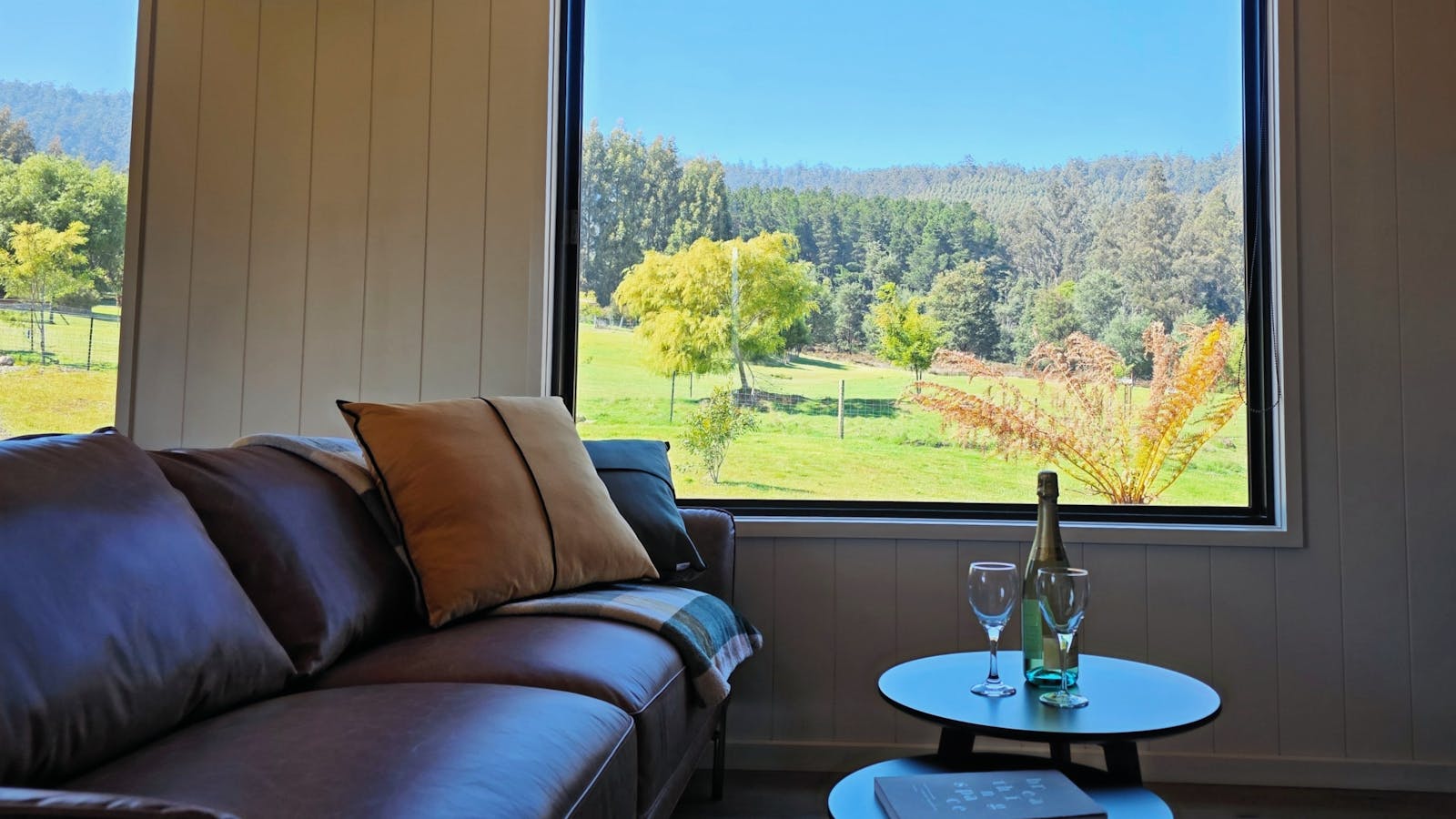 Leather sofa and wool rugs framed by picture windows overlooking neighbour's alpaca farm and forest