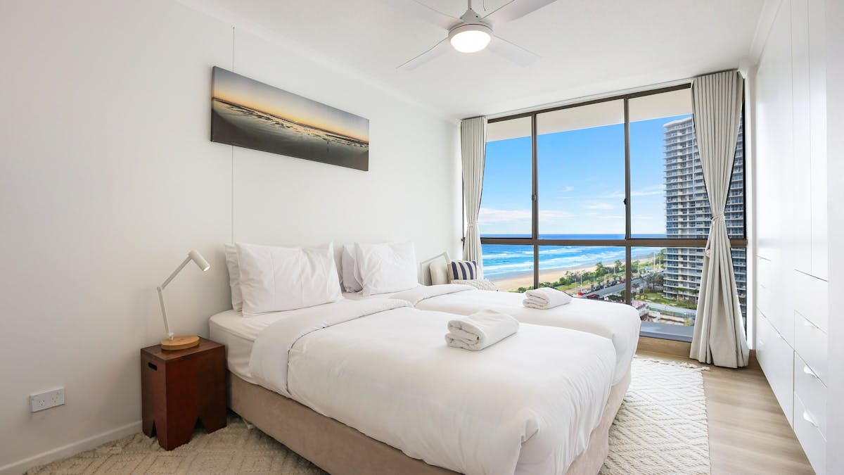 Second bedroom with 2 single beds with floor to ceiling windows on the left side with ocean/ city