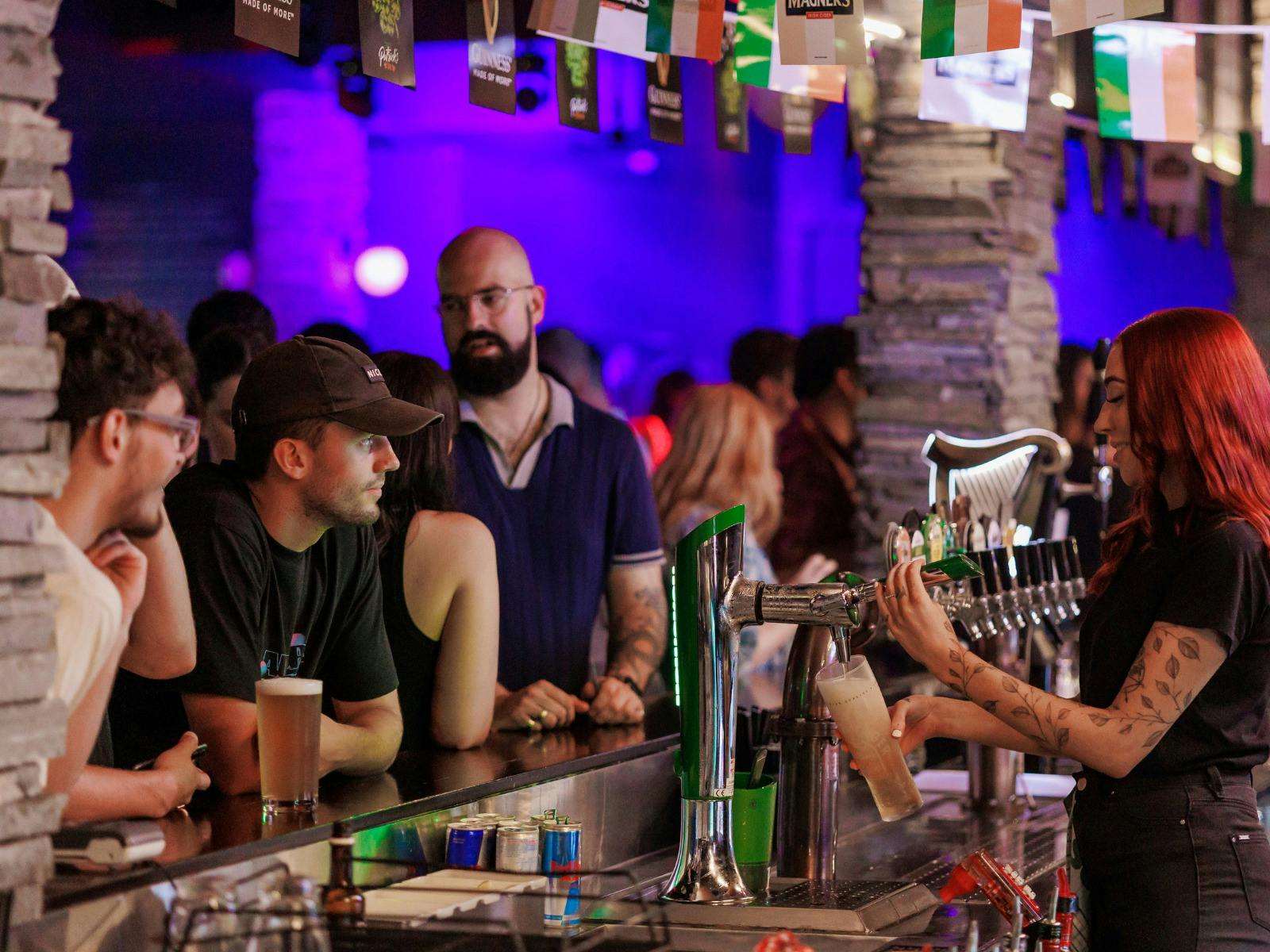 People standing at the bar getting served. Irish flags hanging above them