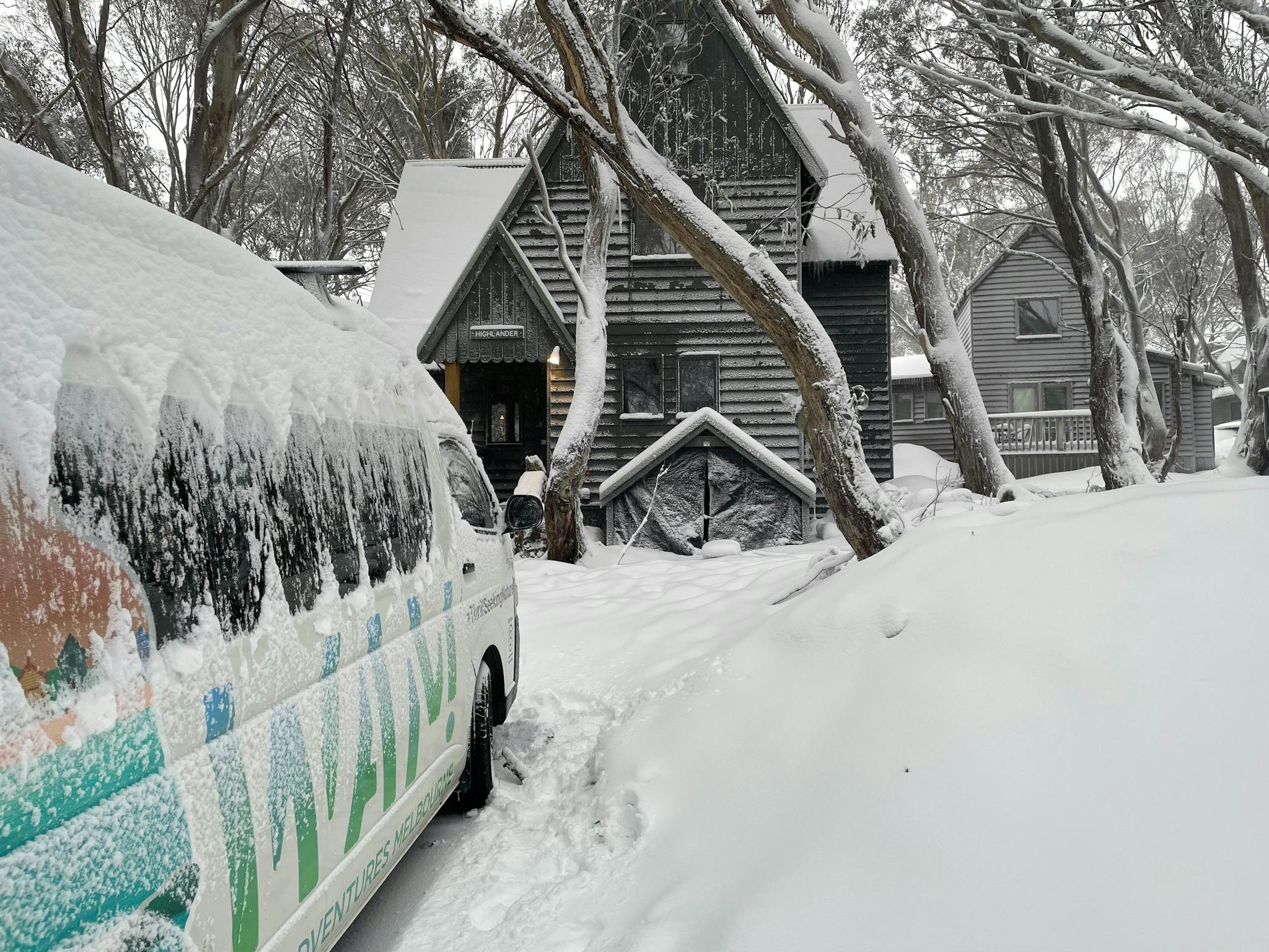 Snow covered vehicle with chalet and snow covered trees in background