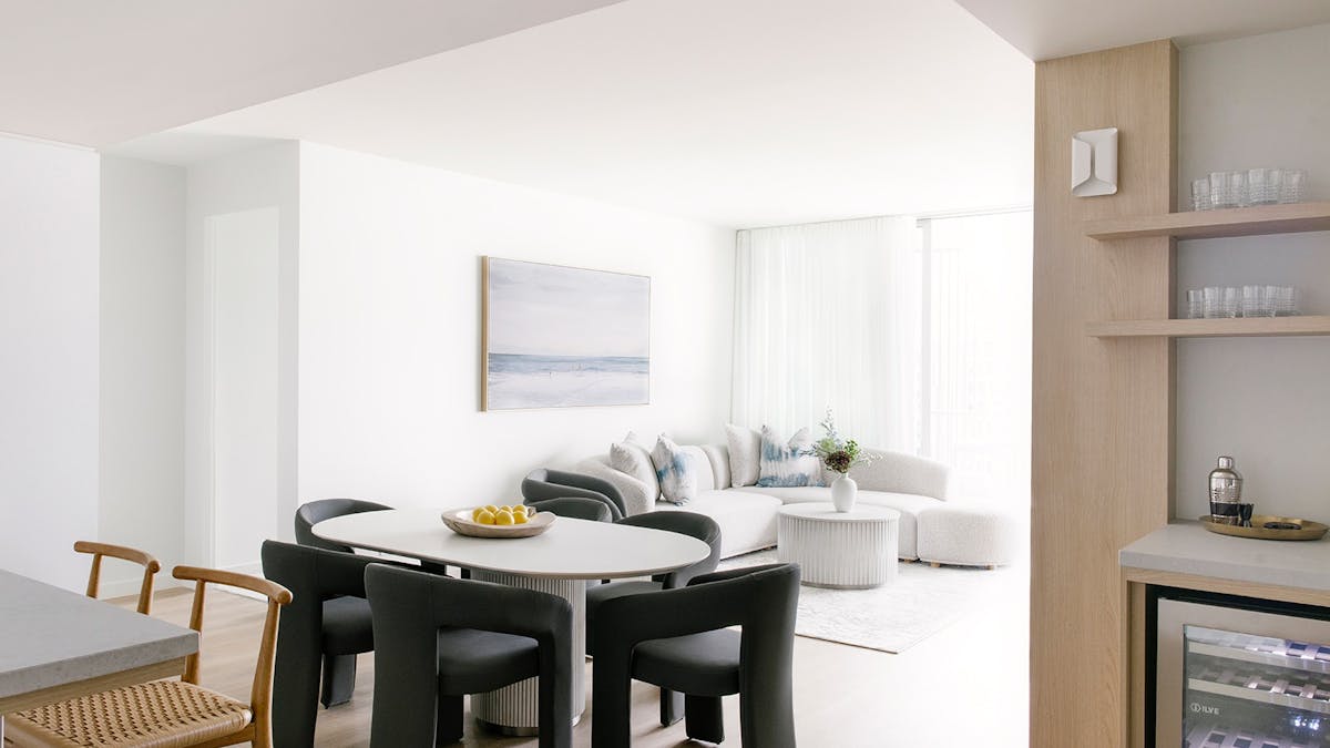 Elegant Kirra Point dining and lounge area with bar fridge, ocean artwork, and soft natural light.